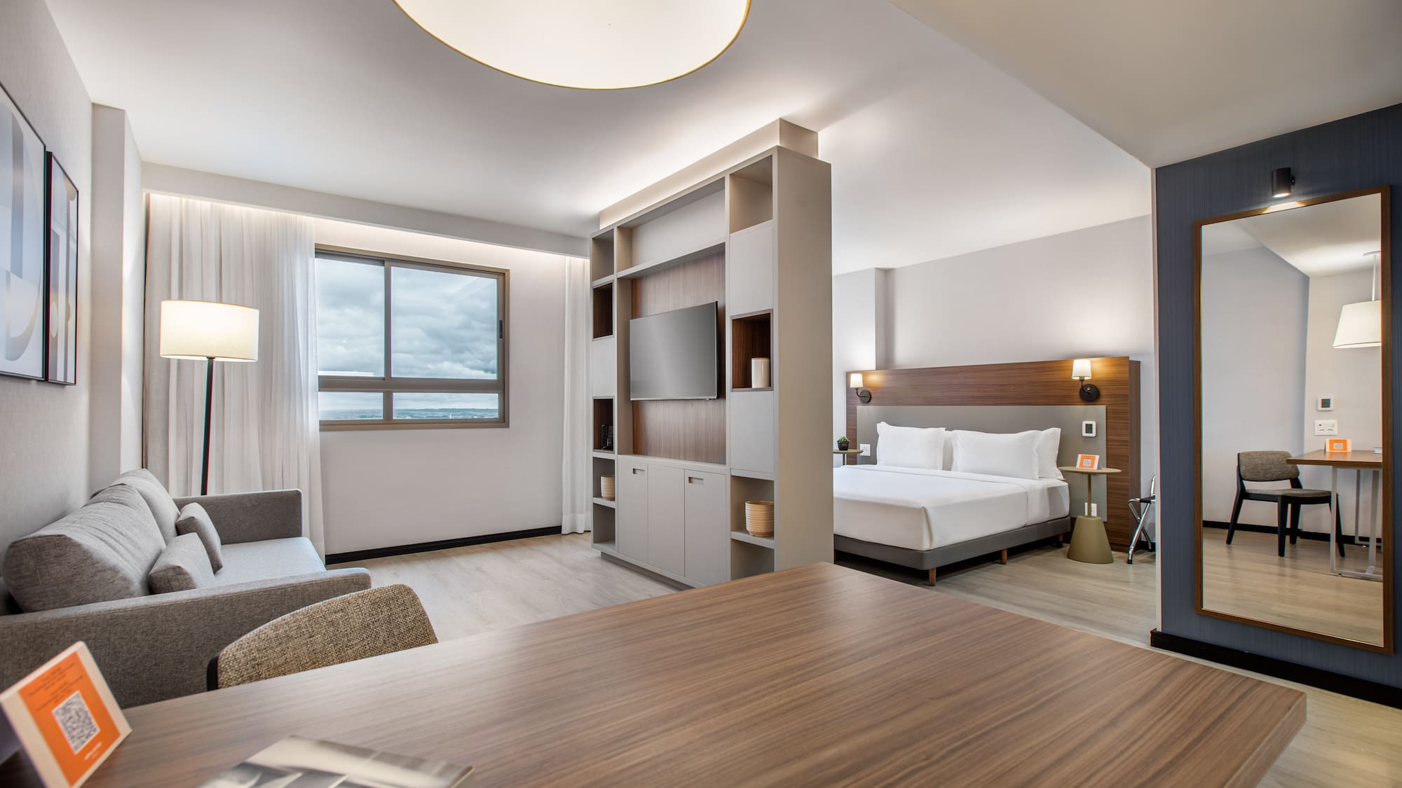 Modern hotel studio suite with bed, sofa, TV, and desk.