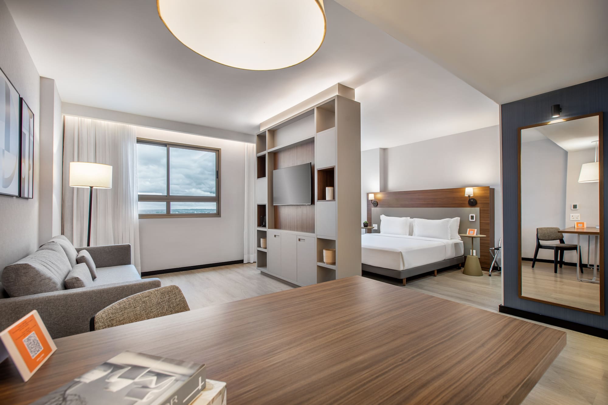 Modern hotel studio suite with bed, sofa, TV, and desk.