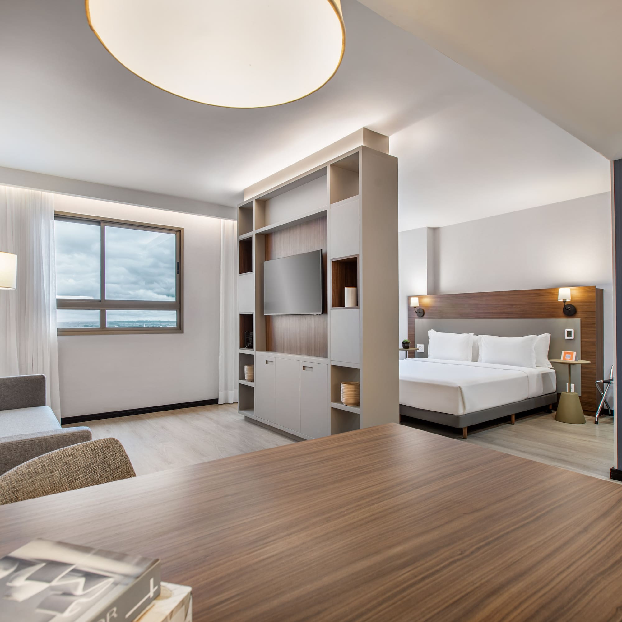 Modern hotel studio suite with bed, sofa, TV, and desk.