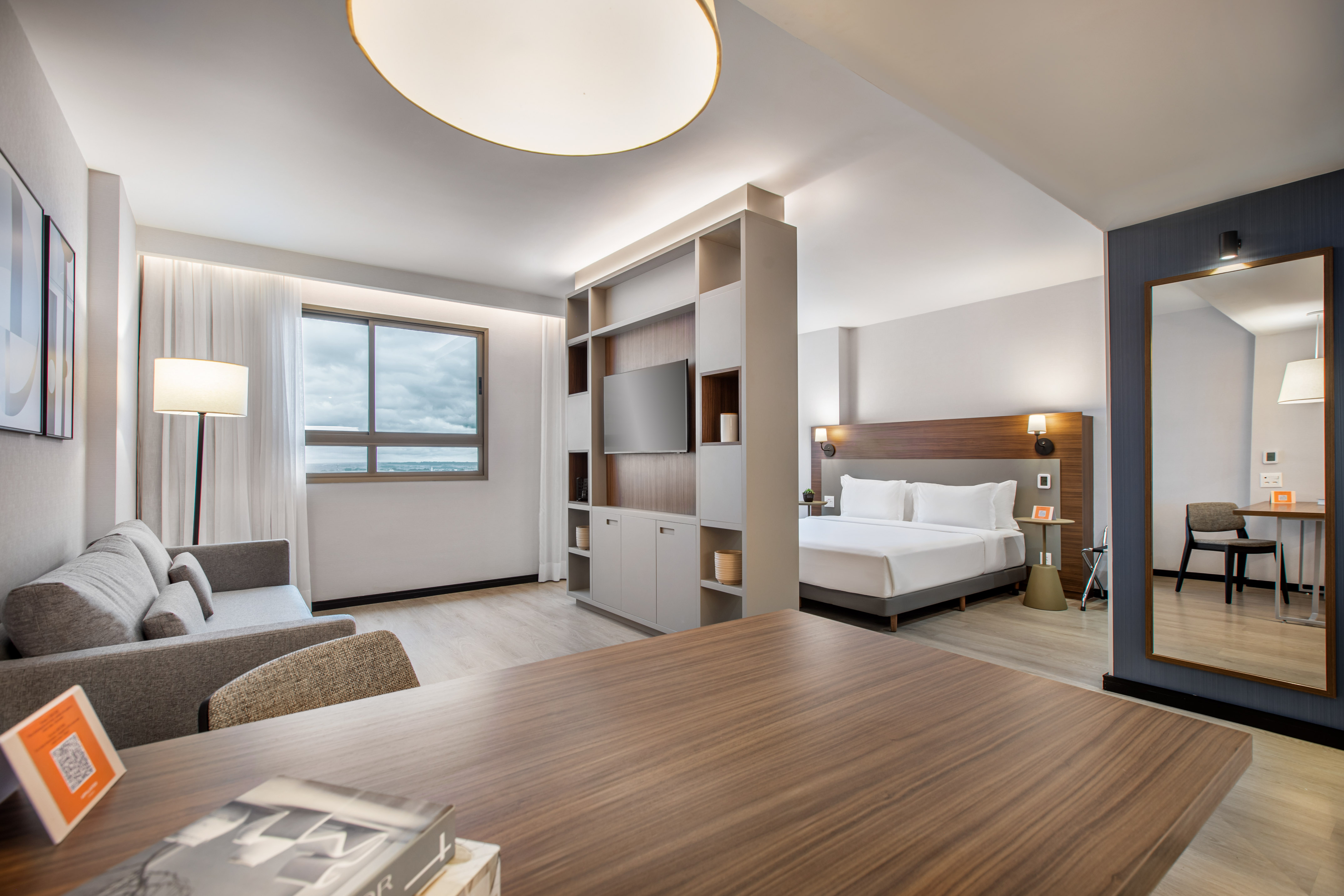 Modern hotel studio suite with bed, sofa, TV, and desk.