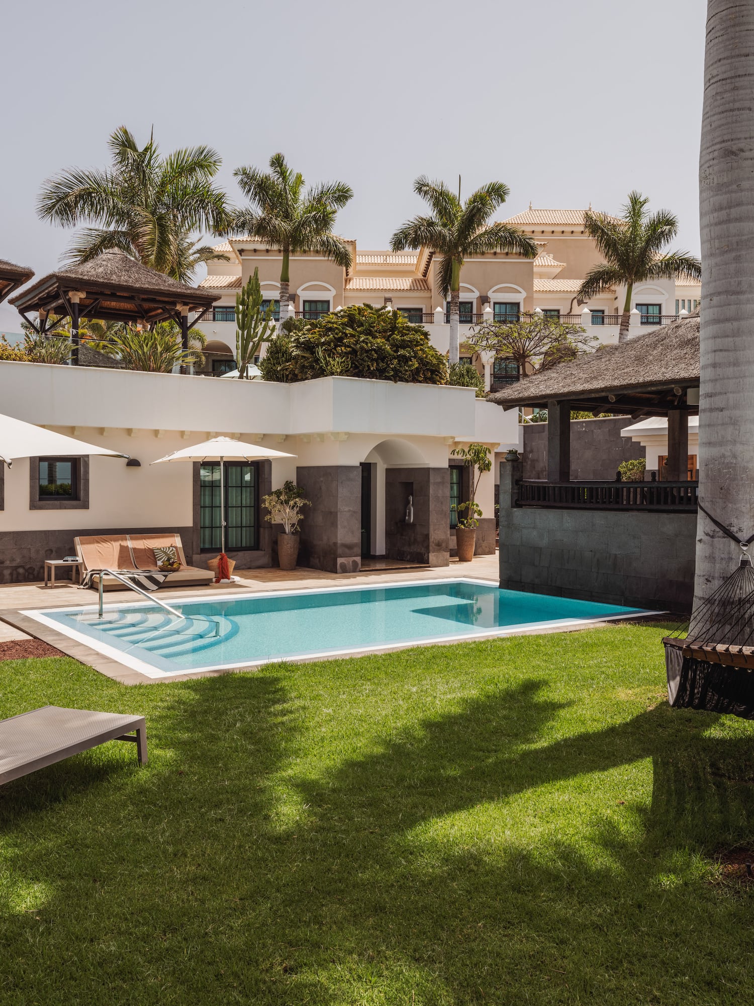 Jardín de villa de lujo con piscina, palmeras, tumbonas y hamaca.