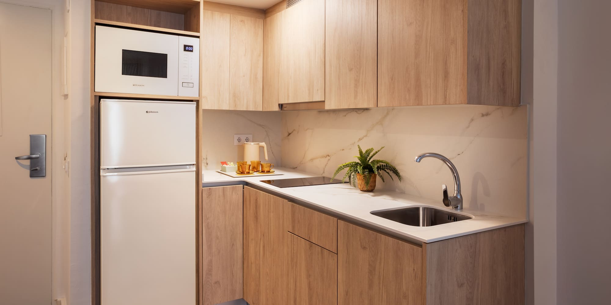 Modern kitchenette with light wood cabinets, white counter, microwave, and fridge.