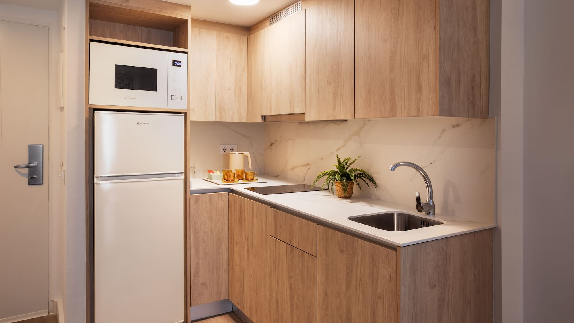 Modern kitchenette with light wood cabinets, white counter, microwave, and fridge.