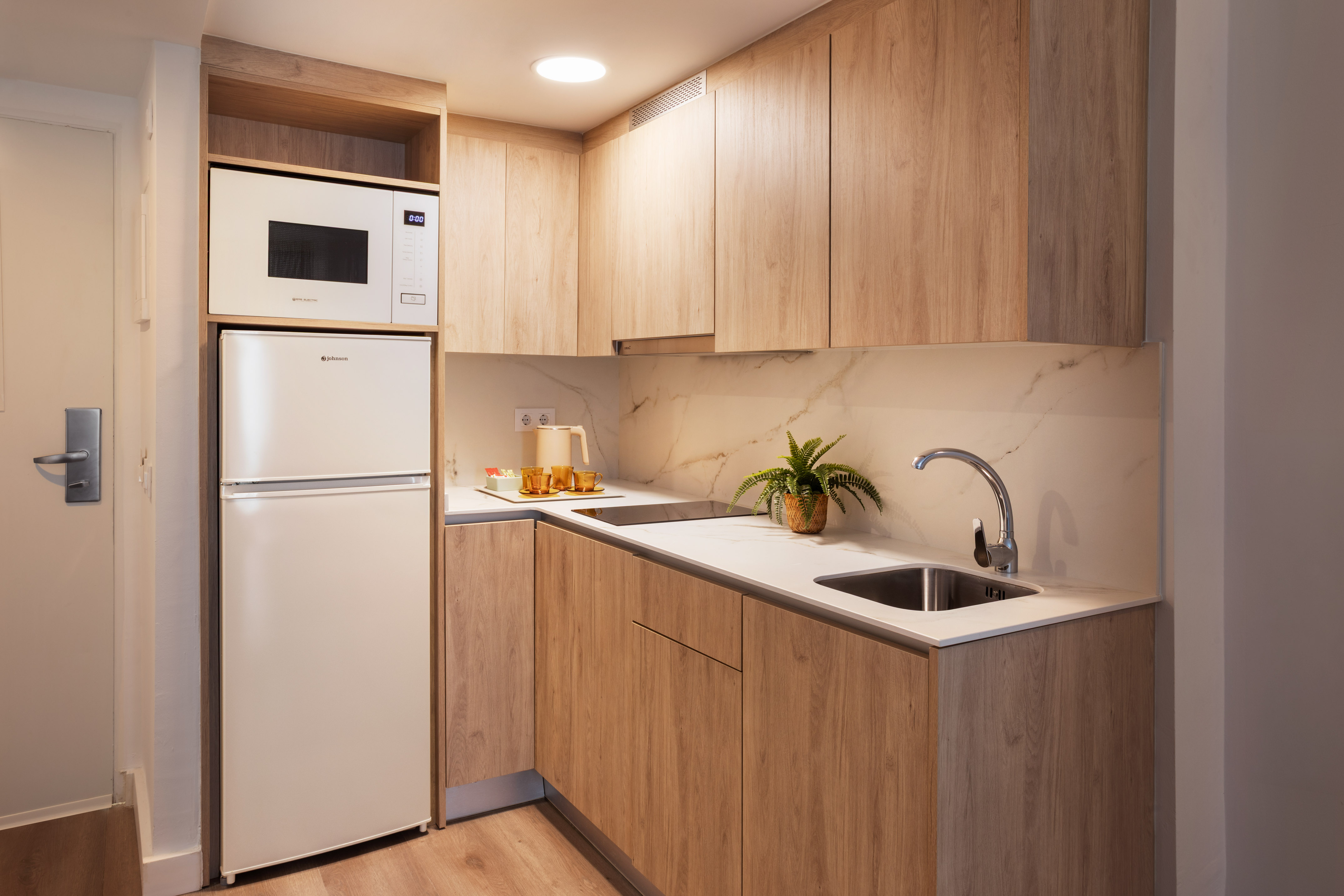 Modern kitchenette with light wood cabinets and white appliances.