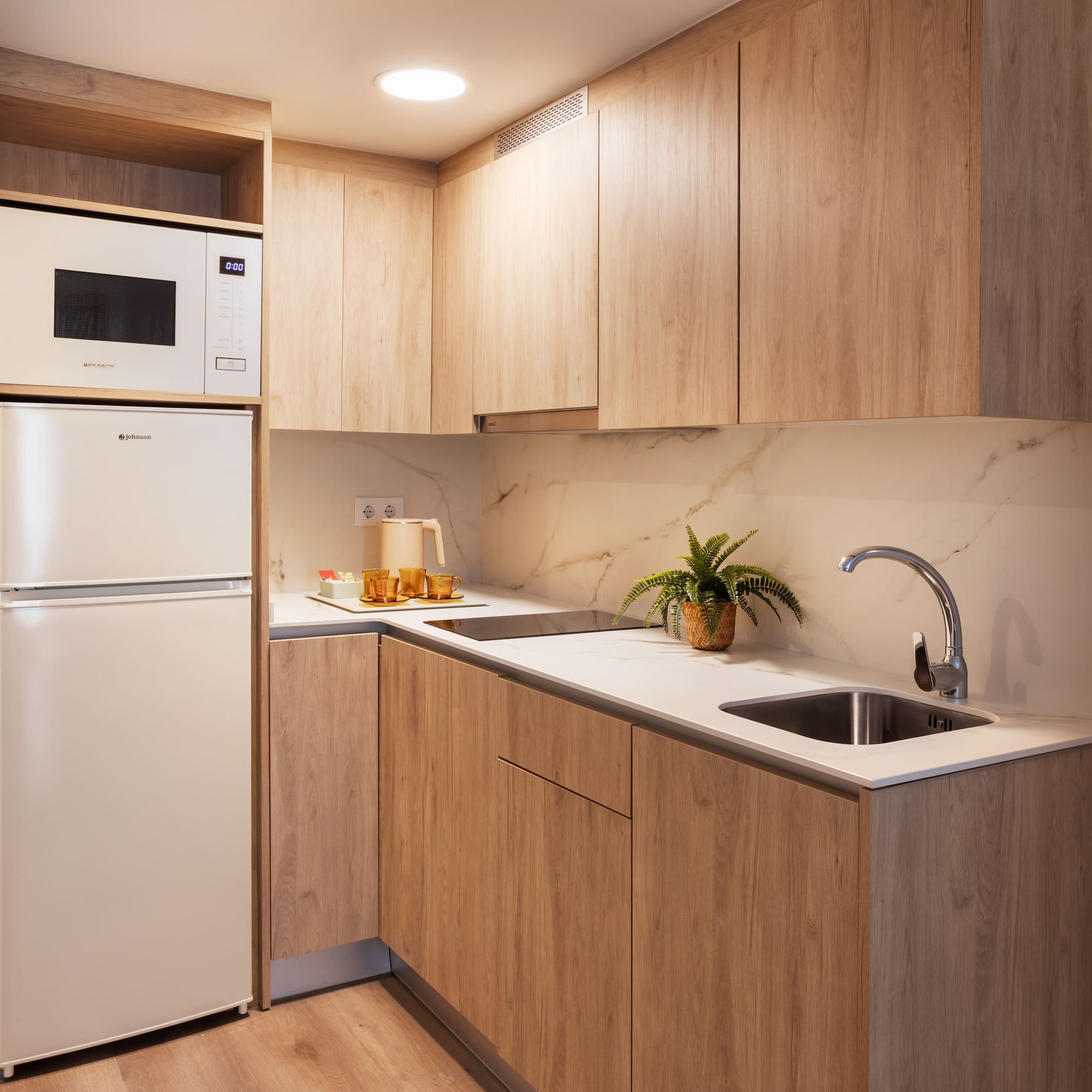 Modern kitchenette with light wood cabinets, white counter, microwave, and fridge.