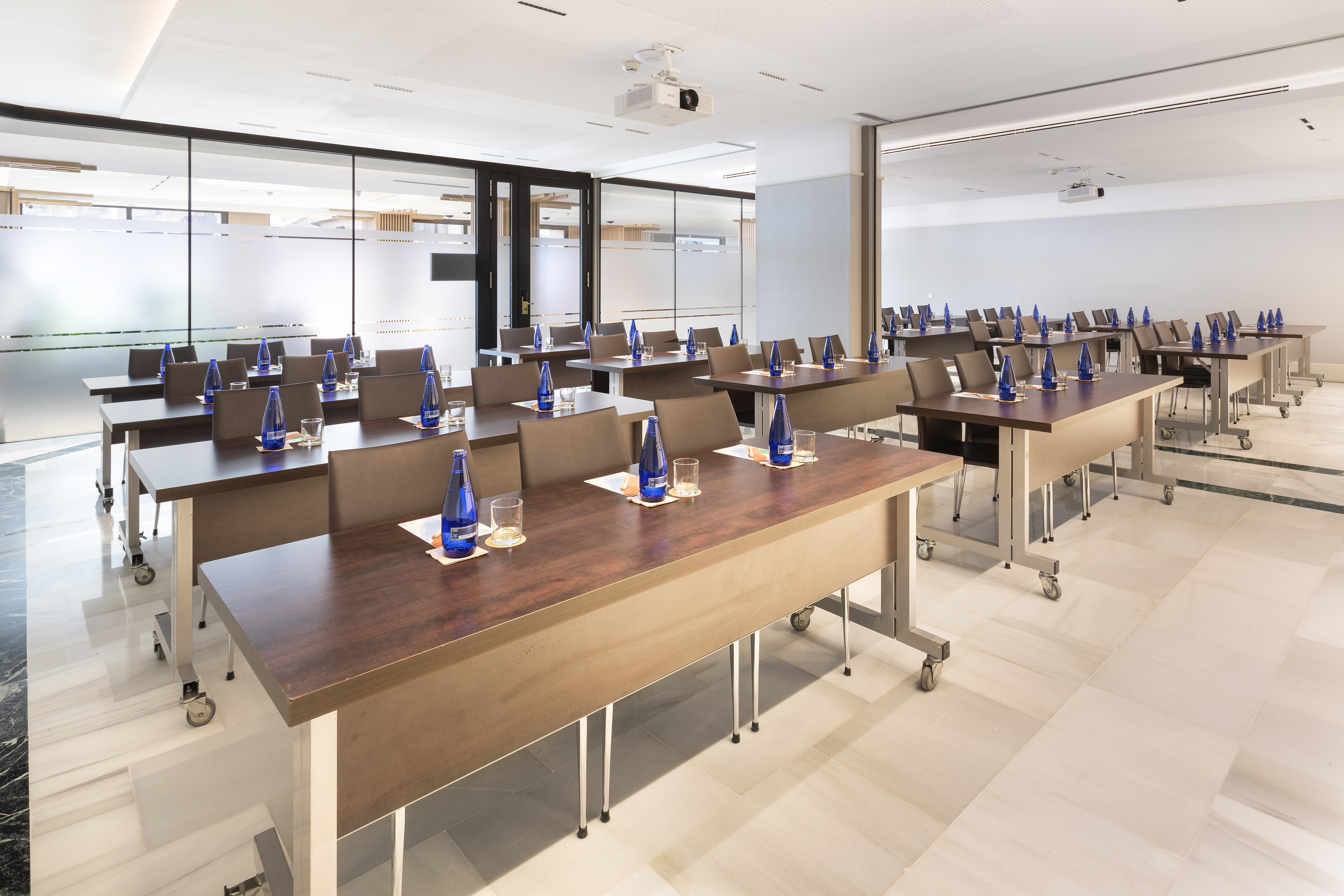 Modern classroom-style conference room with tables, water bottles, and projector.