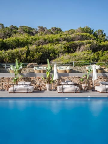 a pool with chairs and umbrellas by a hill