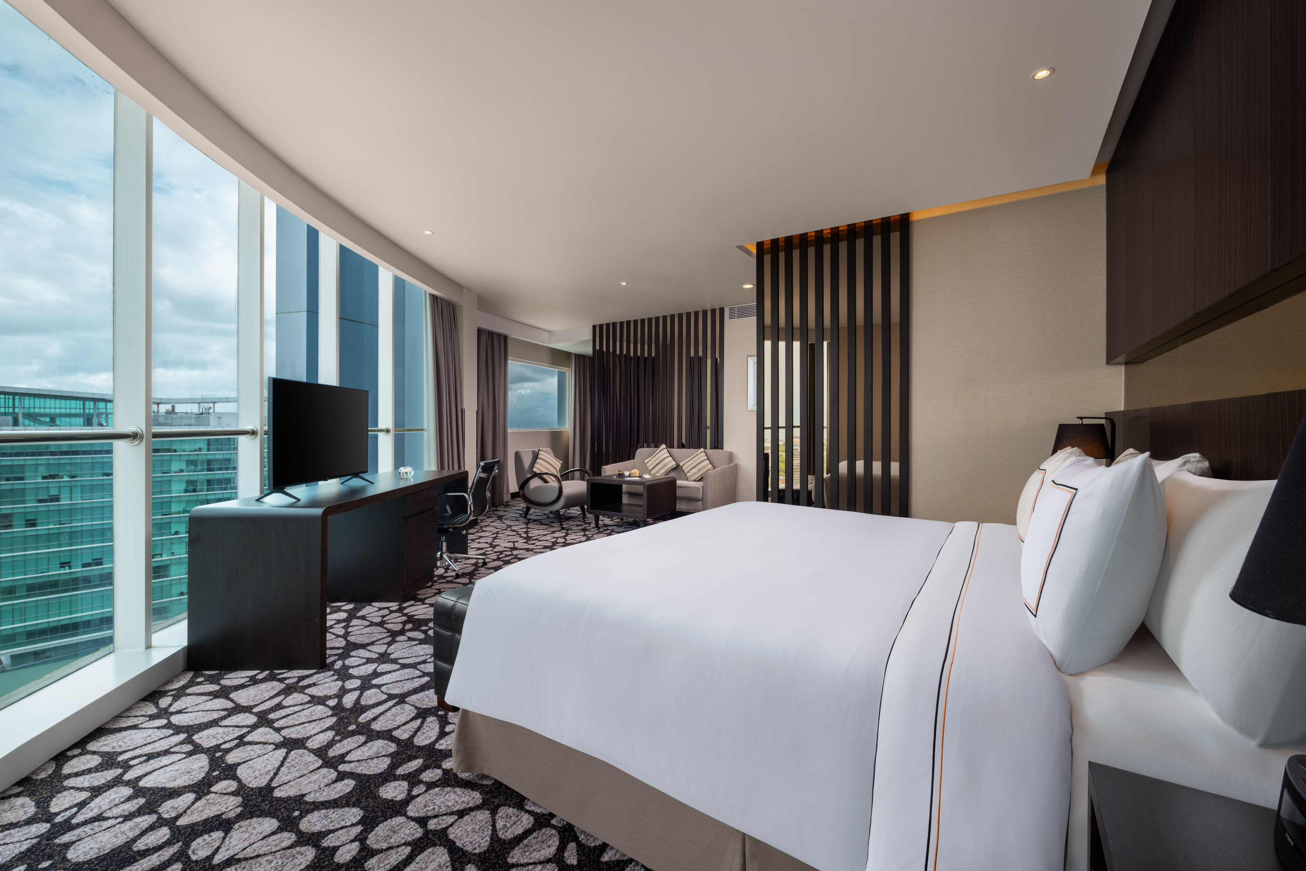 Modern hotel suite with king bed, desk, sofa, and expansive city views.