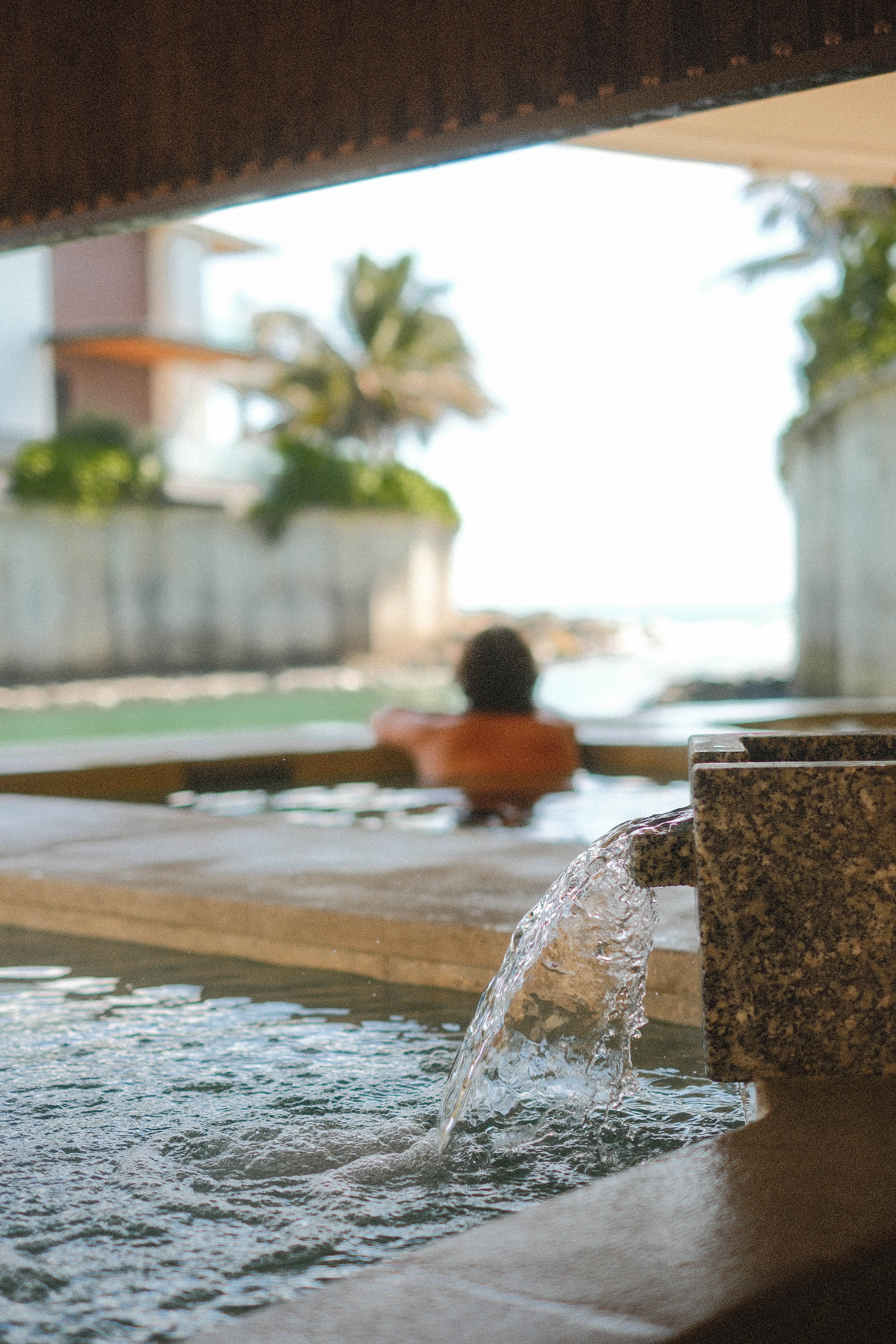 Water flowing into outdoor hot spring with person relaxing, ocean view.