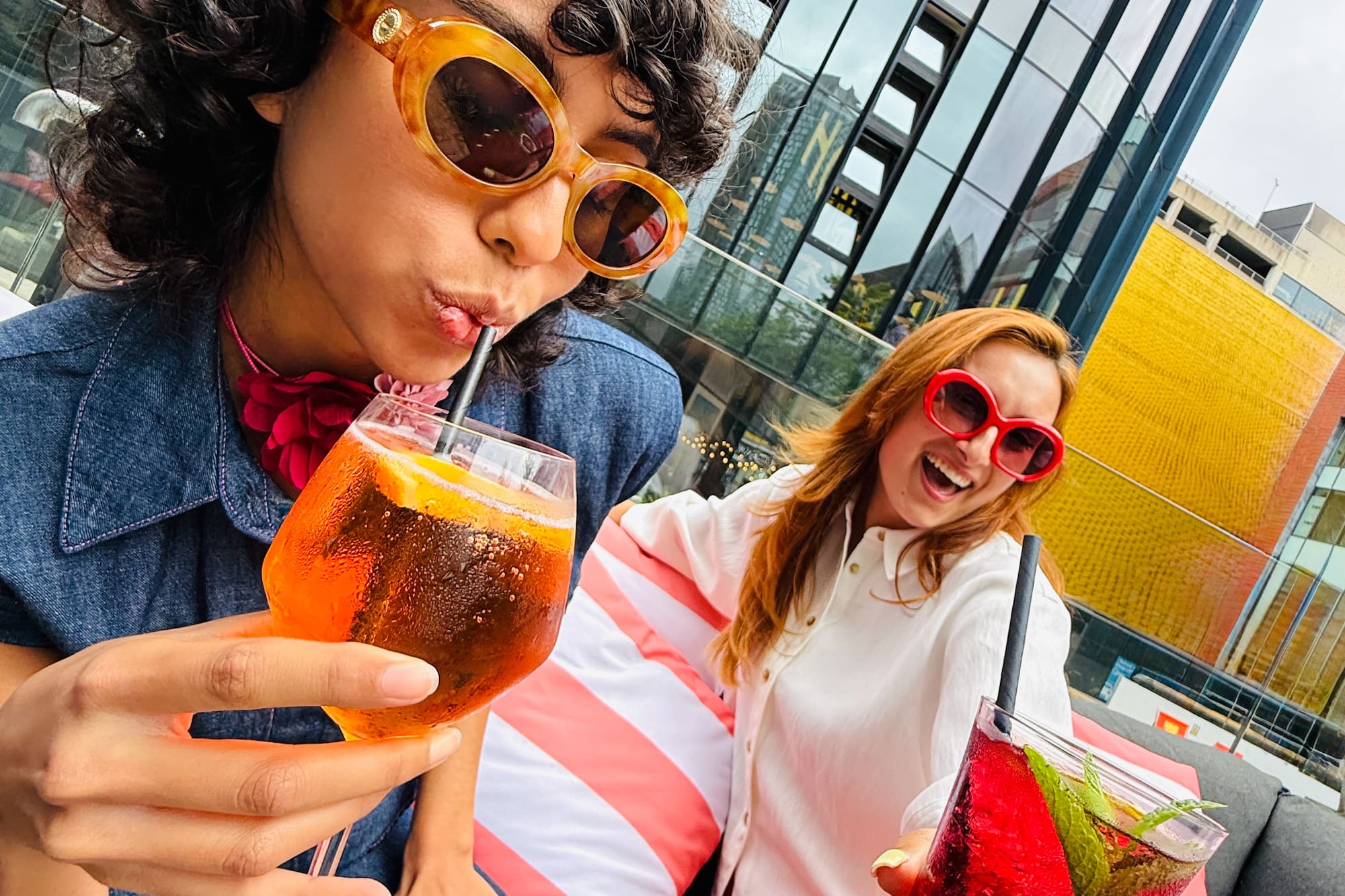 Two friends enjoying colorful cocktails on a vibrant city rooftop.