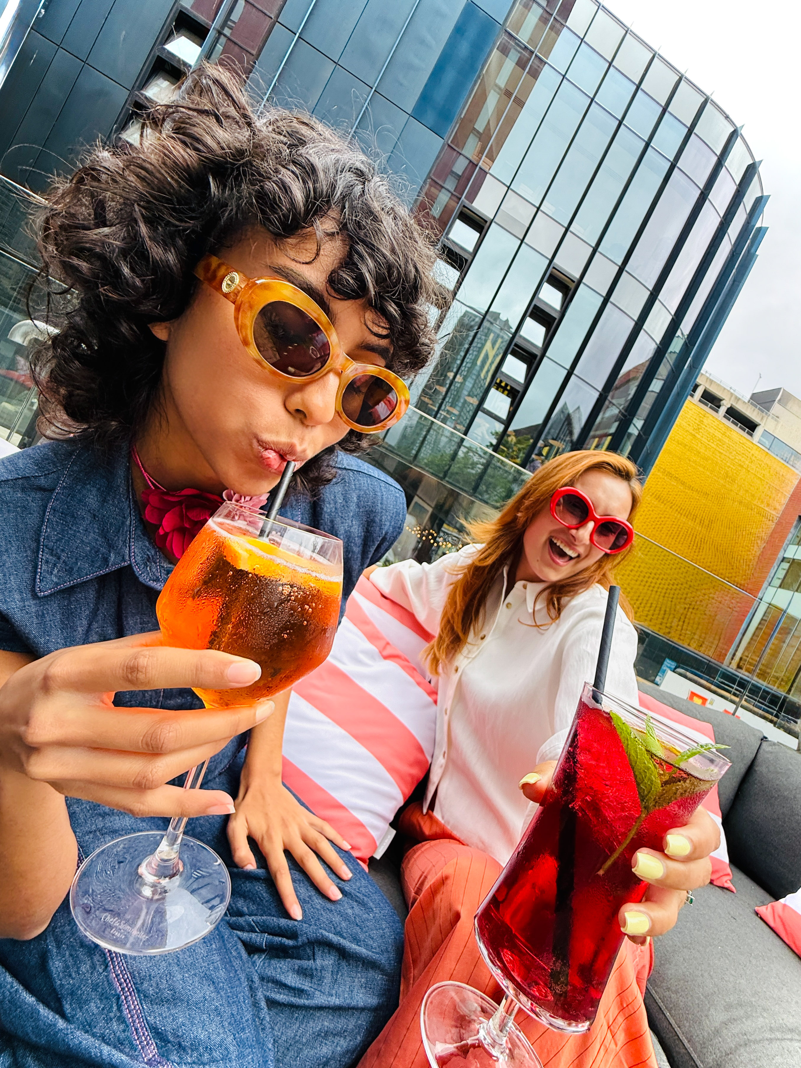 Two friends enjoying colorful cocktails on a vibrant city rooftop.