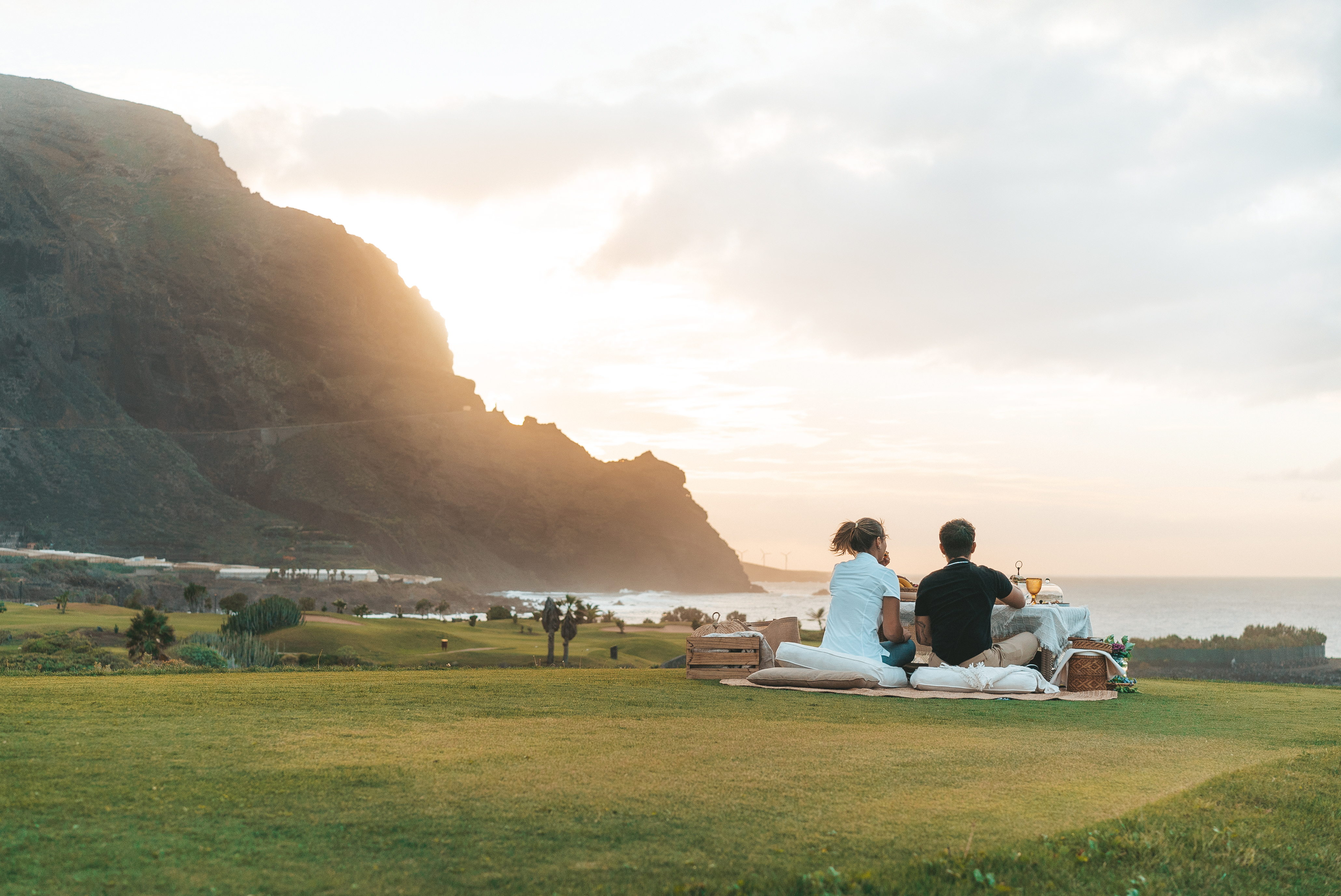 a group of people sitting on a blanket on a grassy field