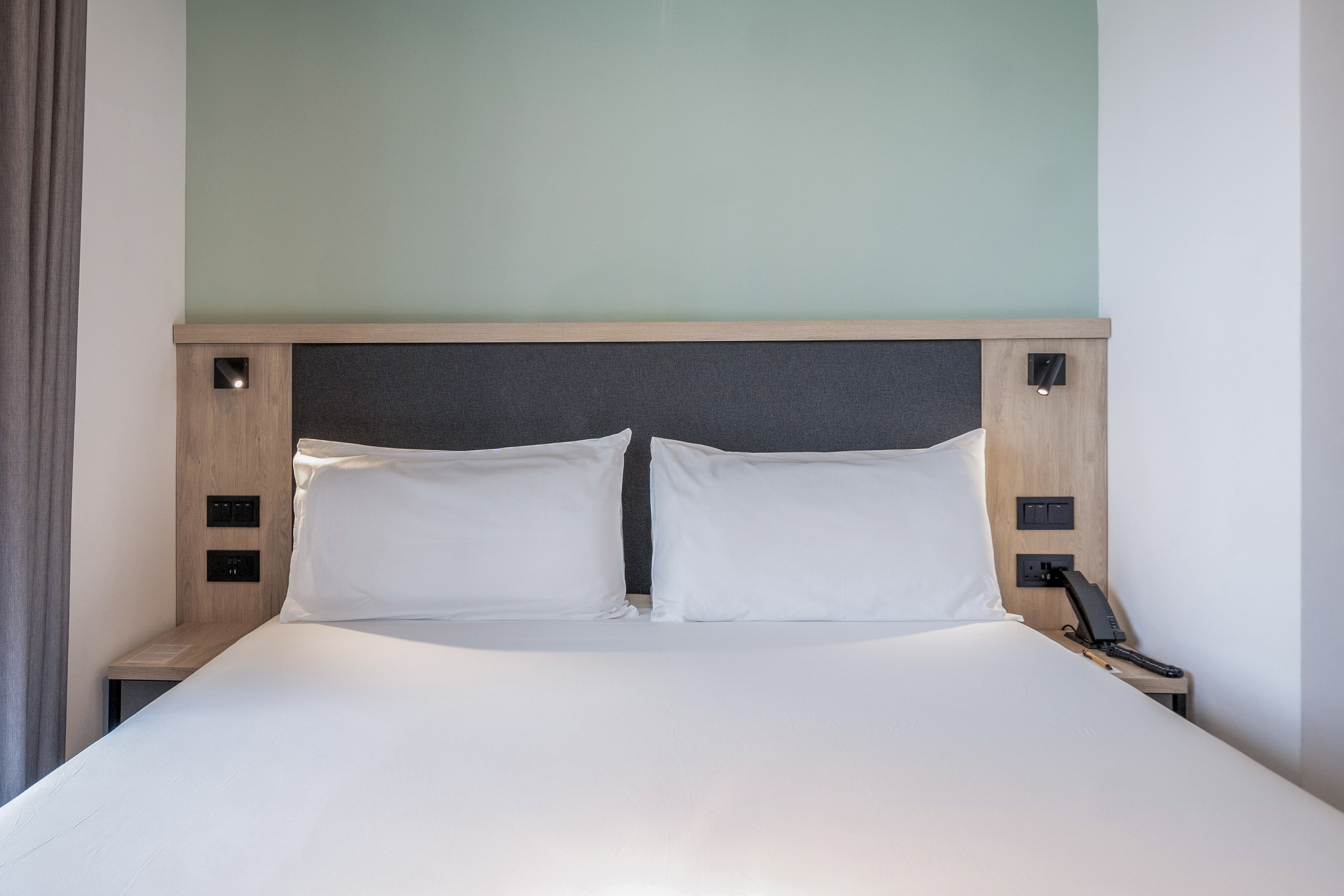 Clean hotel bed with white sheets, dark headboard, and integrated bedside lights.