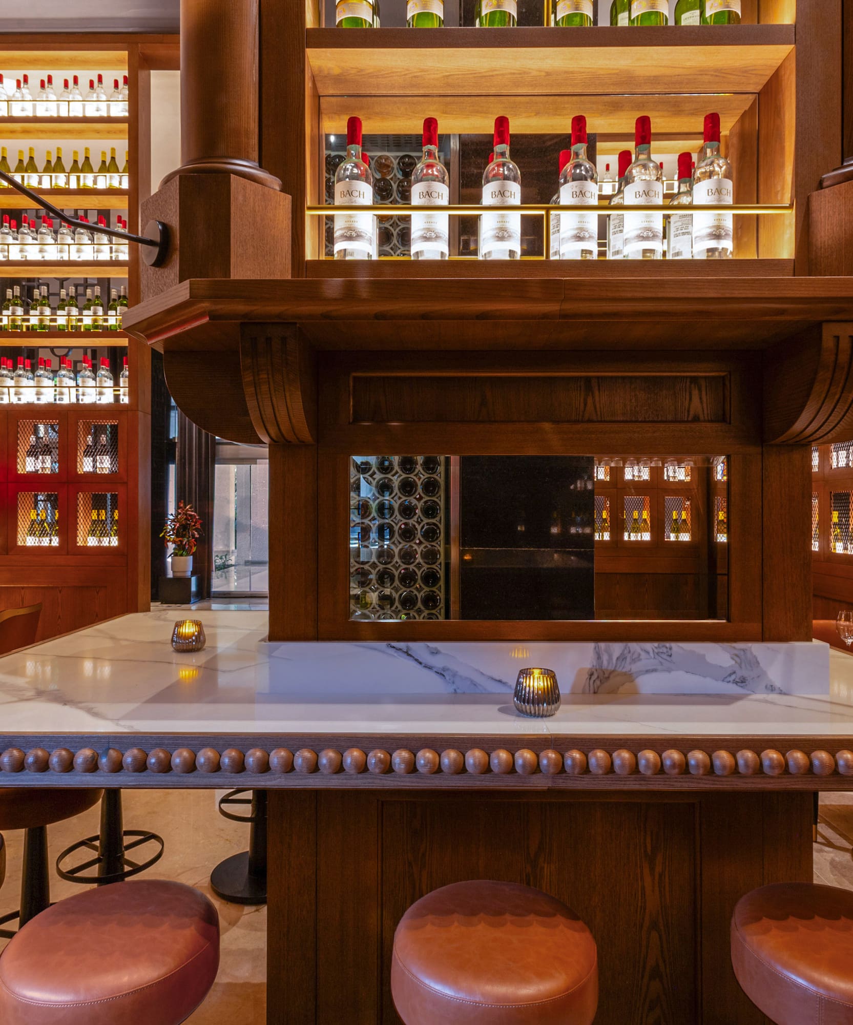 Elegant bar with wooden wine bottle displays, marble counter, and leather stools.