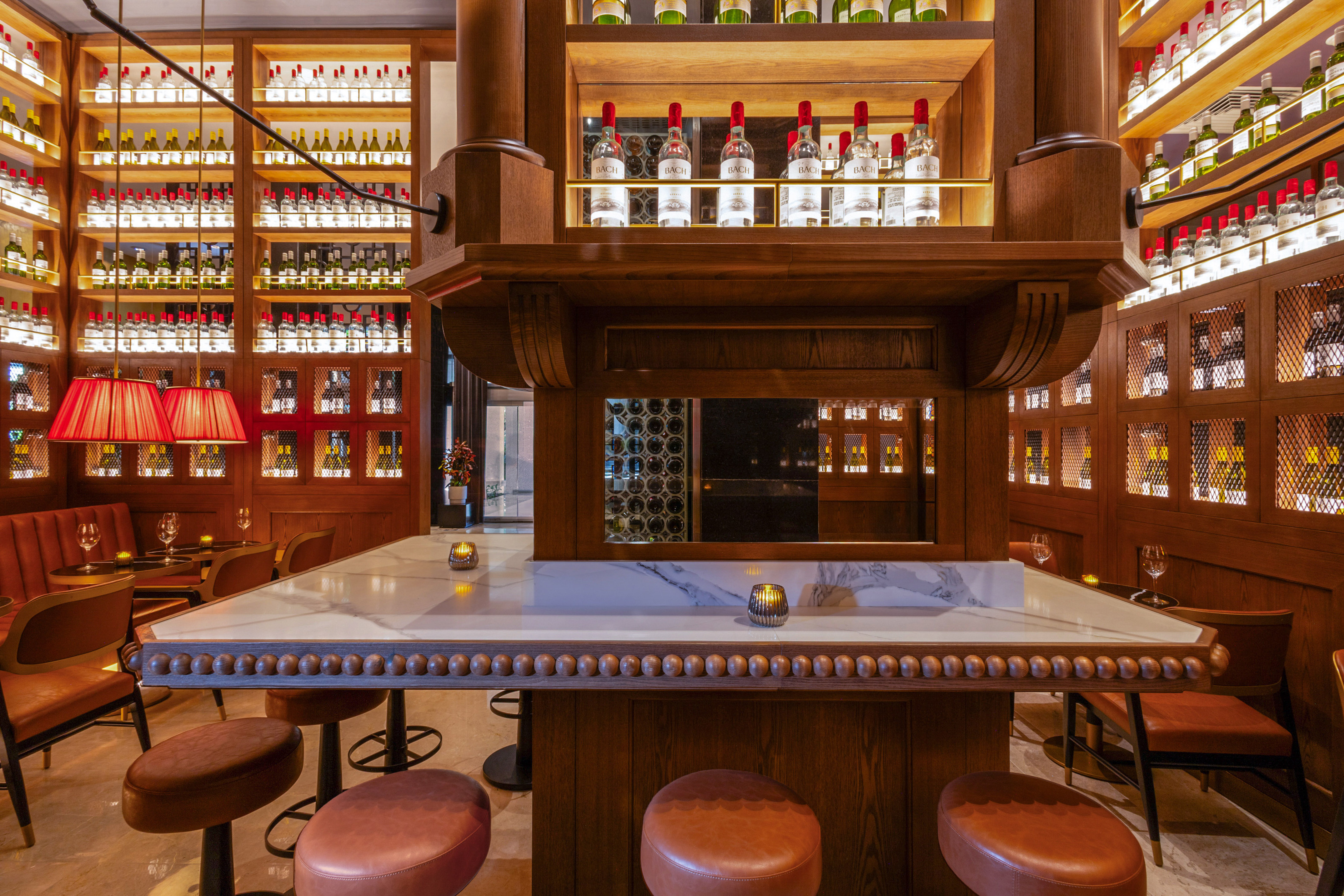 Upscale bar with wine bottles, wood shelves, marble counter, and leather stools.