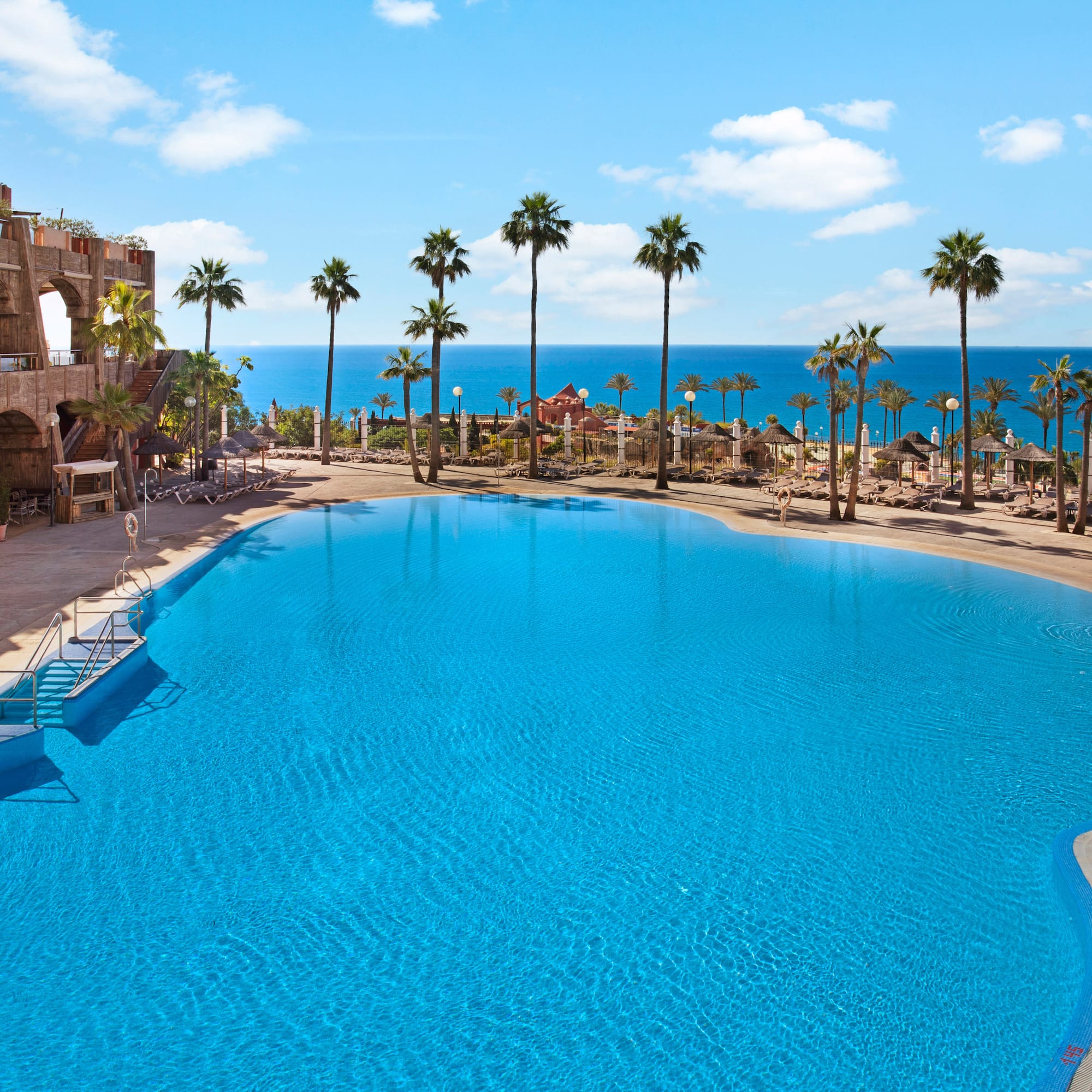 a pool with palm trees and a beach and a body of water