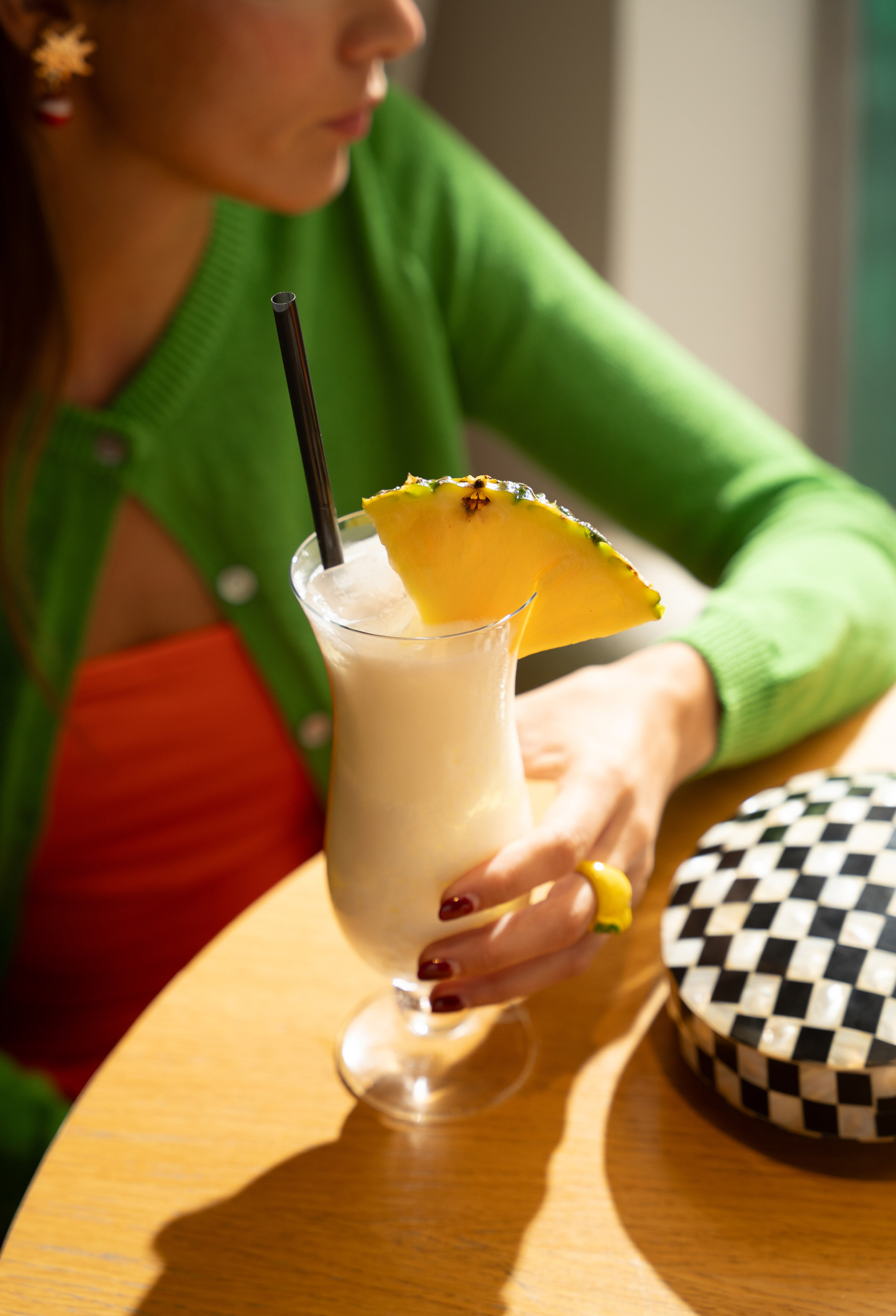 Woman holding a piña colada with pineapple garnish and straw on wooden table.
