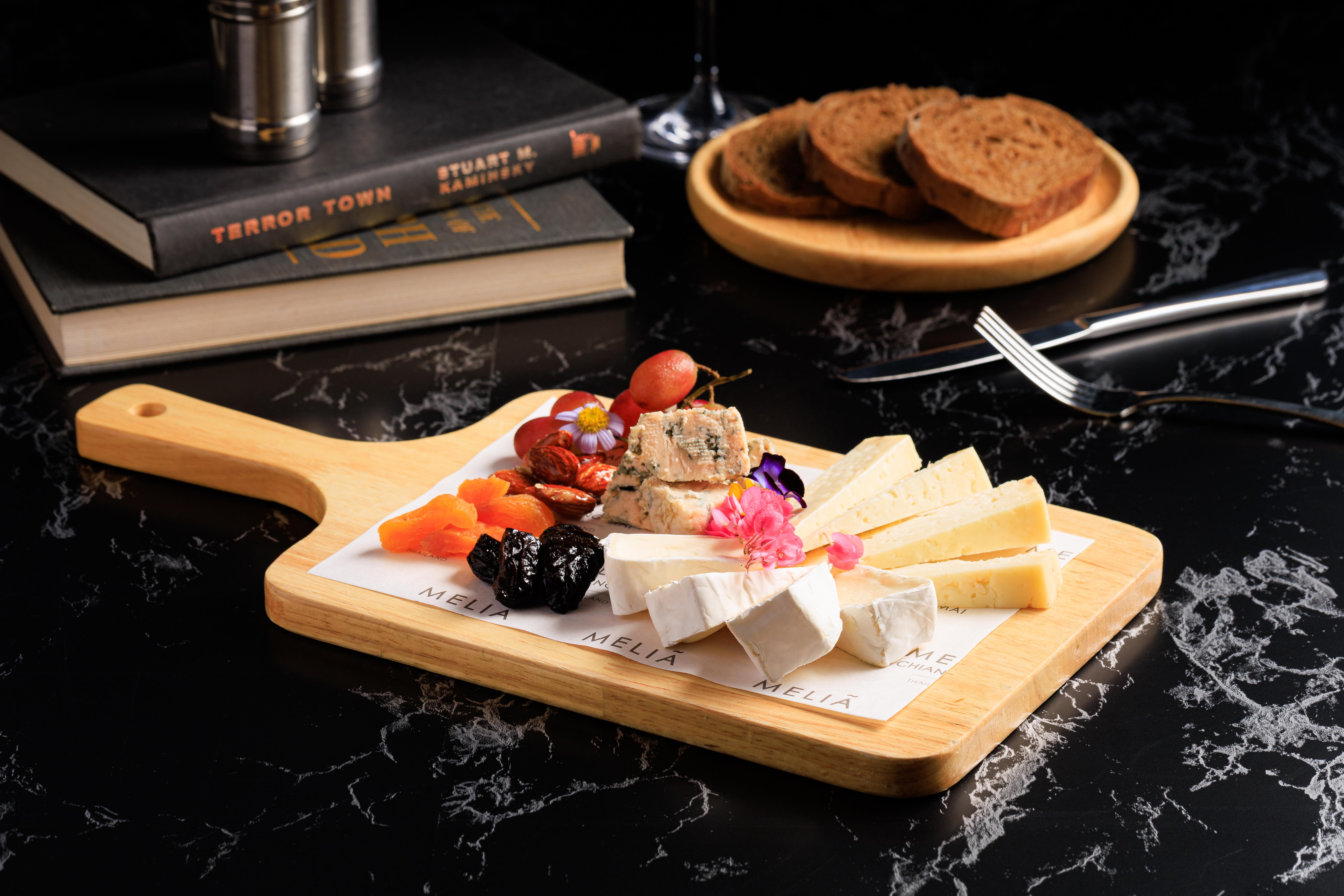 Gourmet cheese board with brie, blue cheese, dried fruit, nuts, bread on marble.