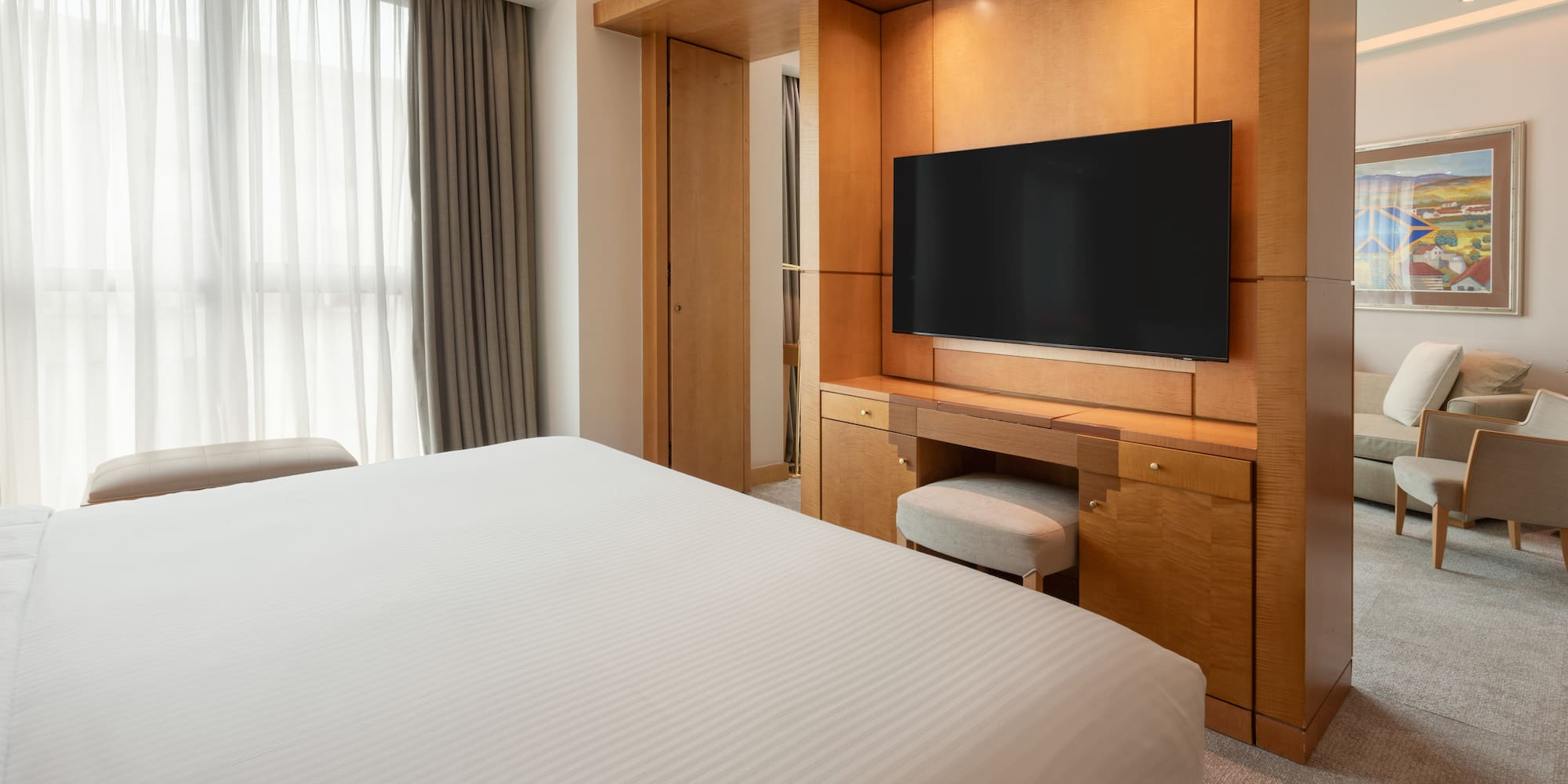 Luxury hotel room with bed, wooden TV console, and lounge area.