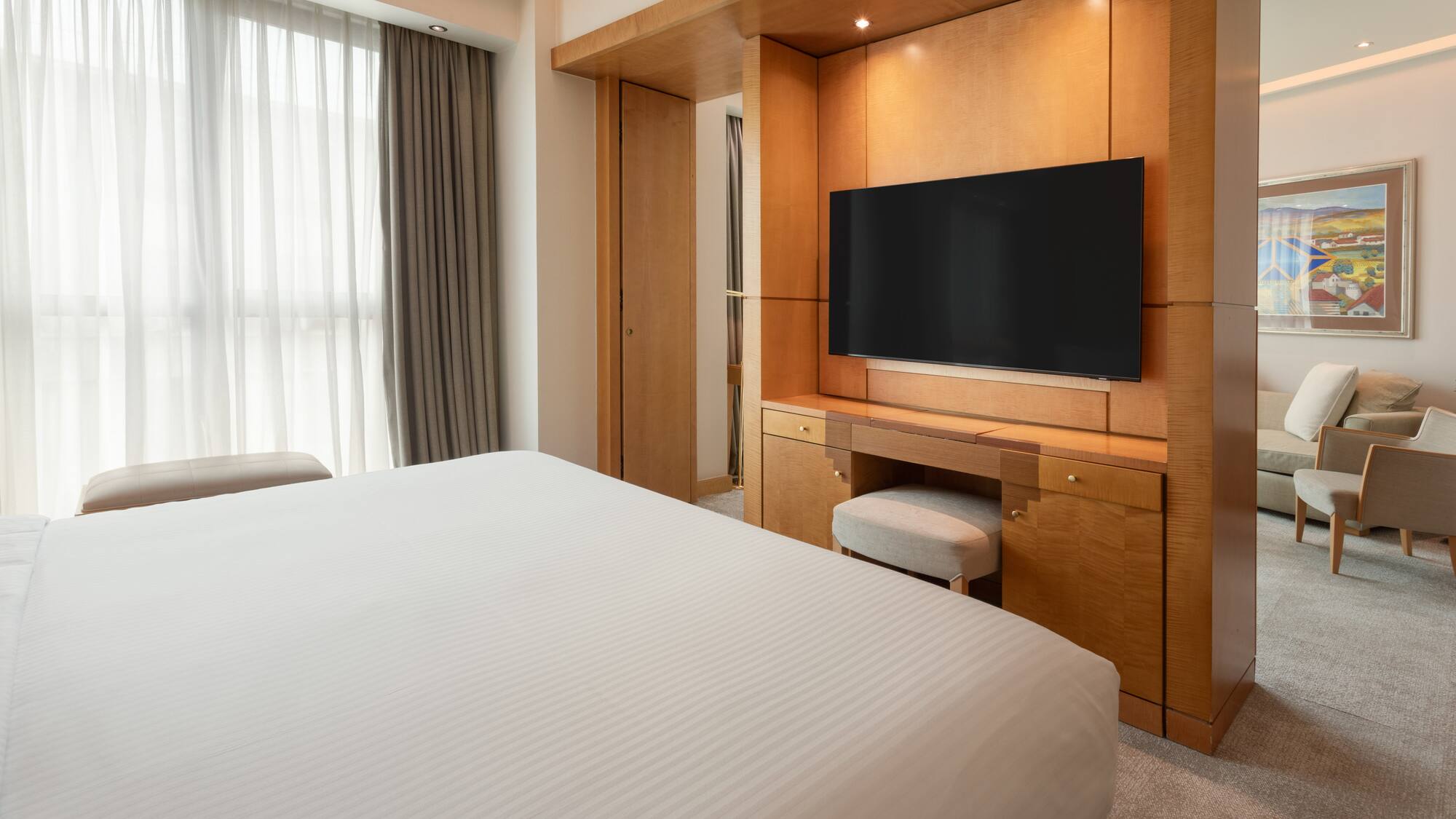 Luxury hotel room with bed, wooden TV console, and lounge area.