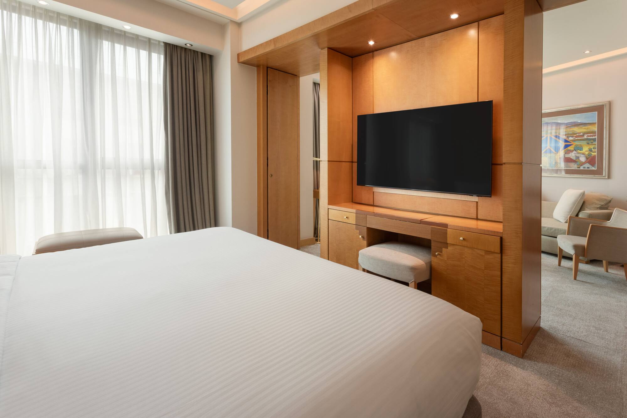 Luxury hotel room with bed, wooden TV console, and lounge area.