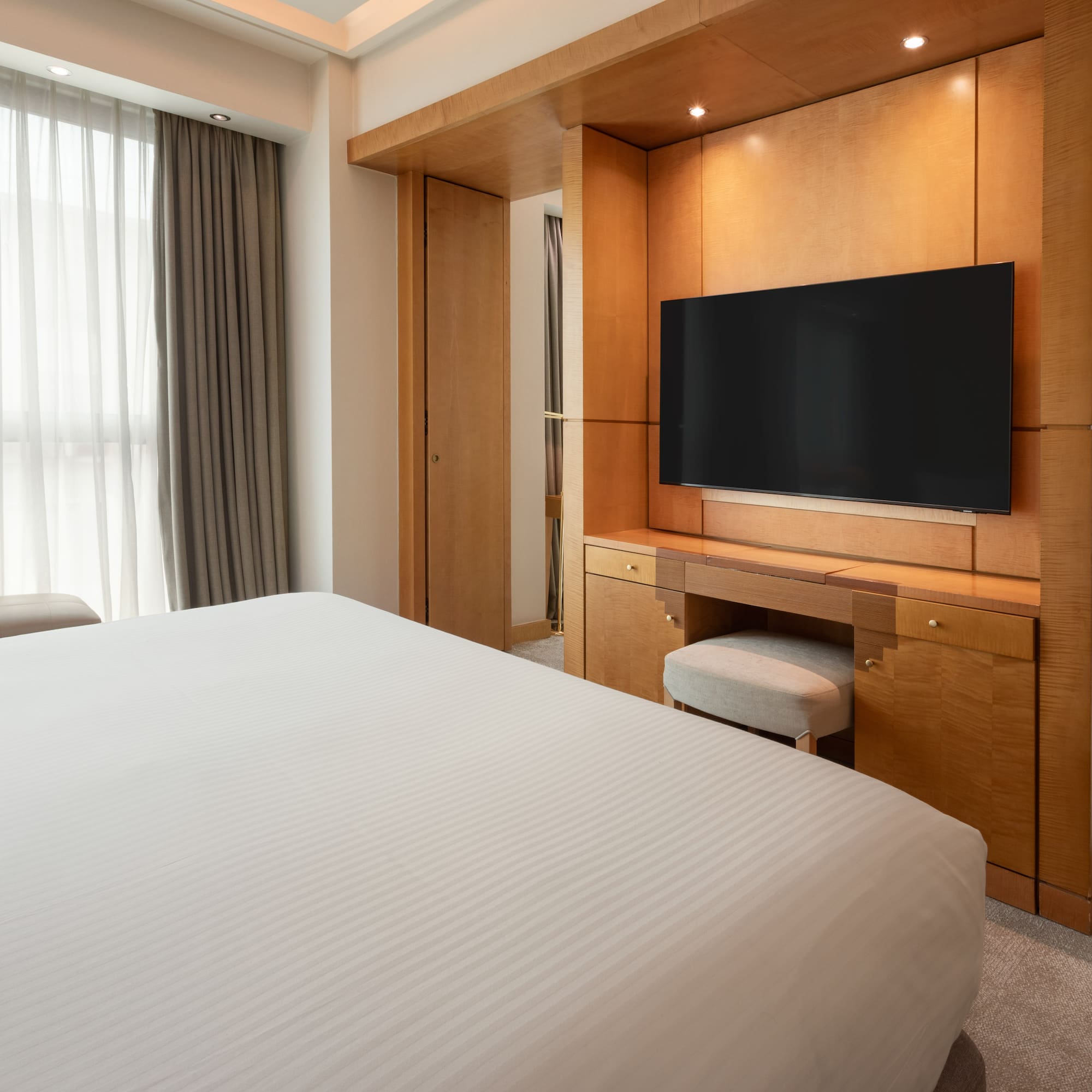 Luxury hotel room with bed, wooden TV console, and lounge area.