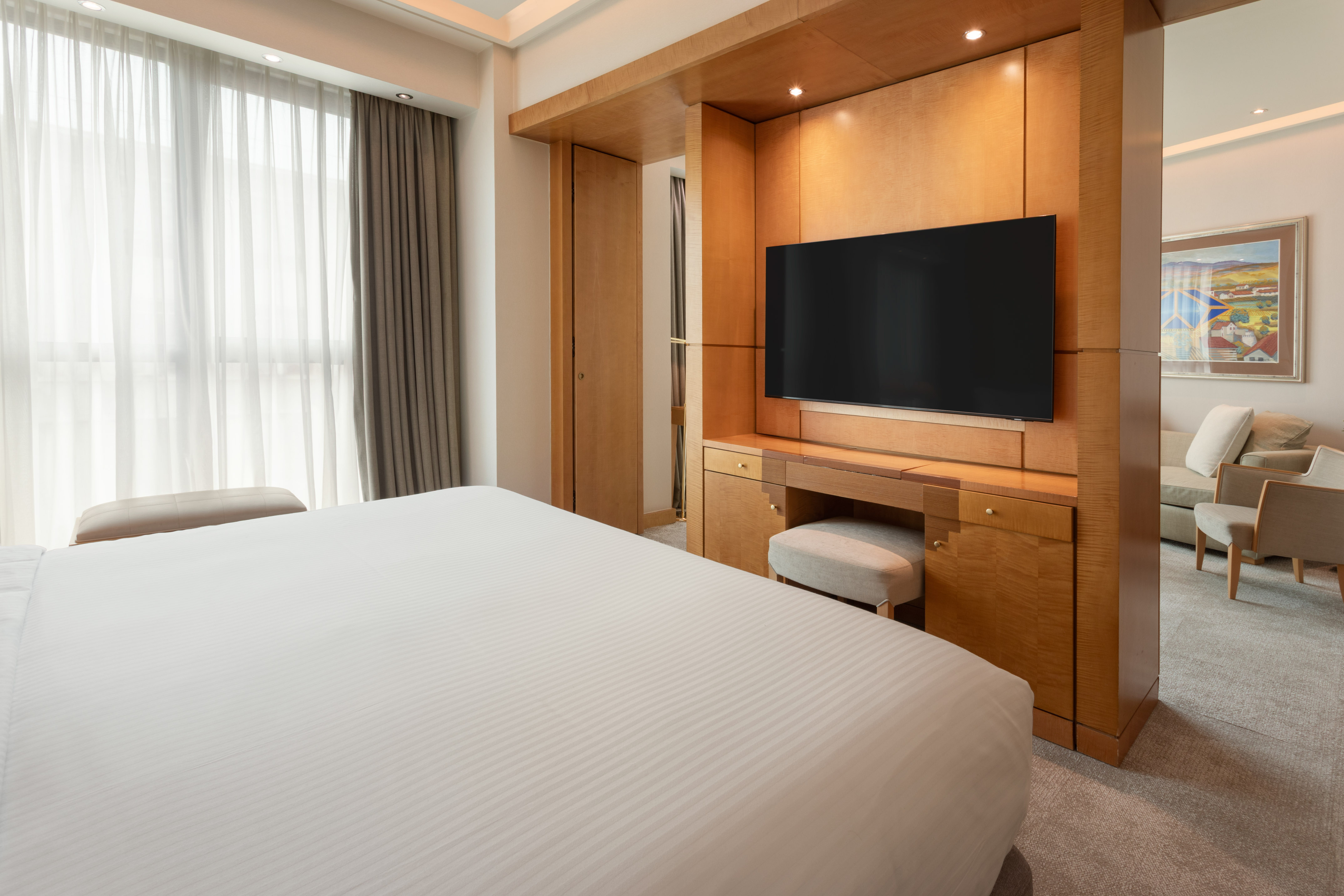 Luxury hotel room with bed, wooden TV console, and lounge area.