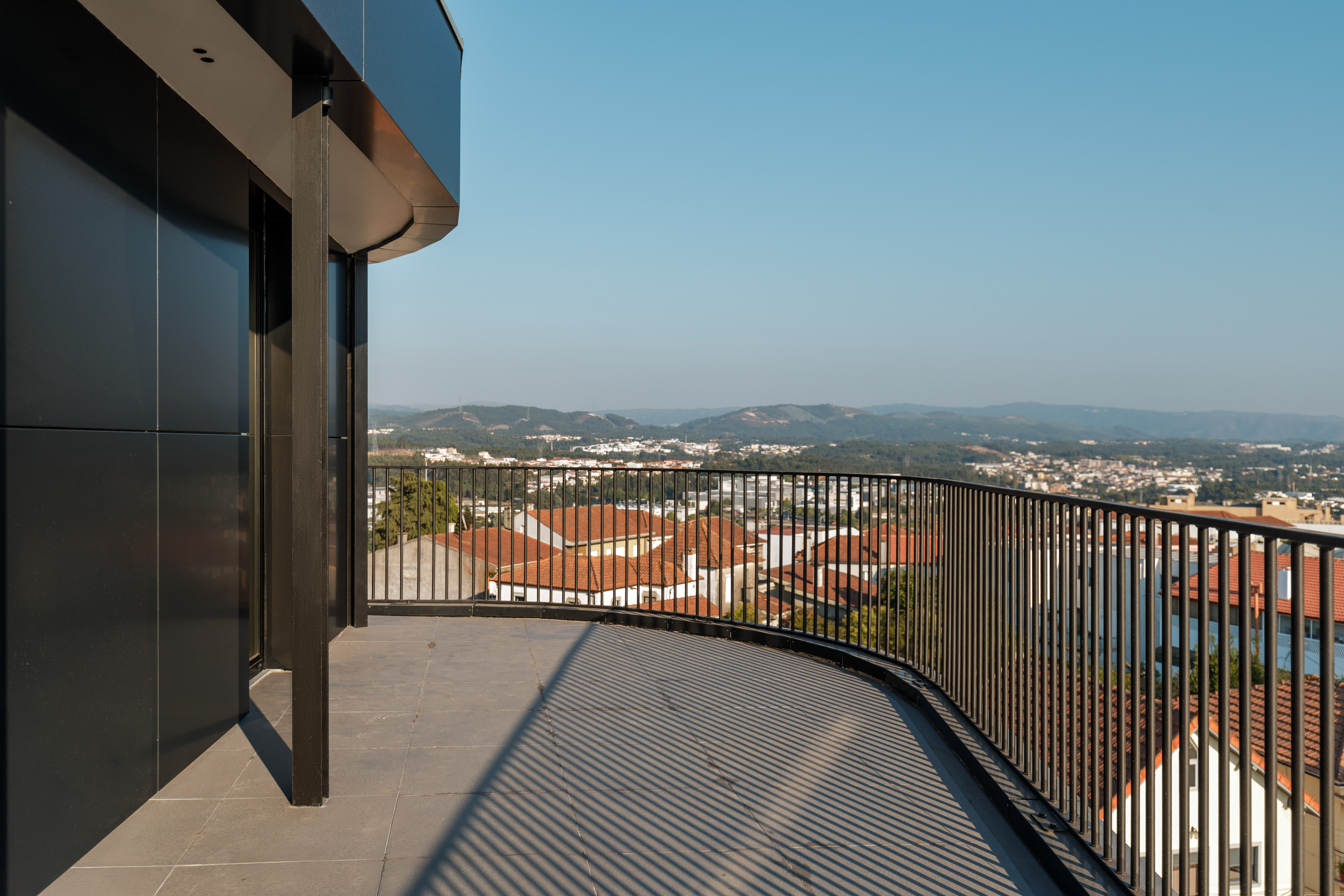 Modern curved balcony with black railing and panoramic city view.