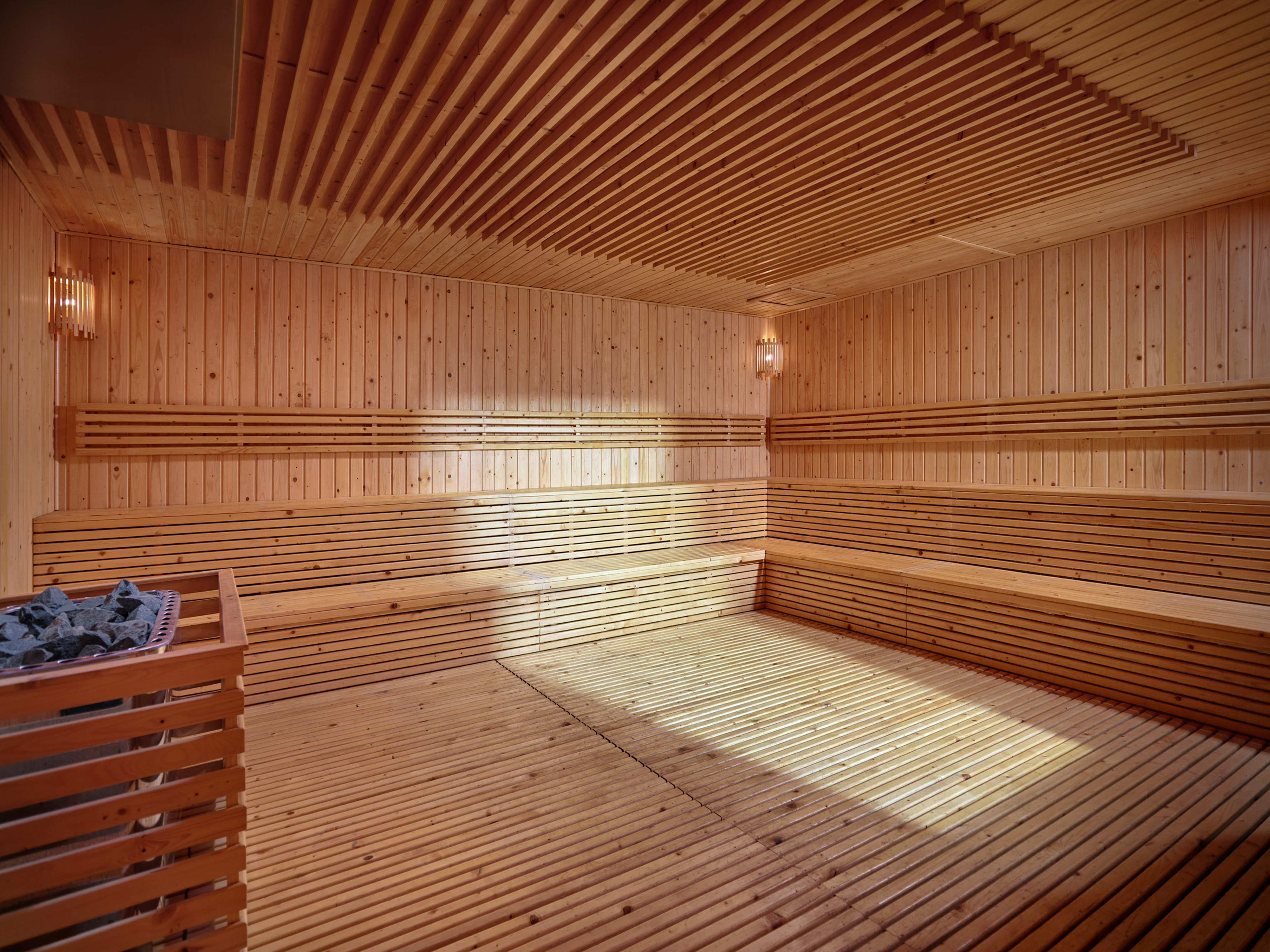 Wooden sauna room with slatted walls, benches, floor, ceiling, and heater.