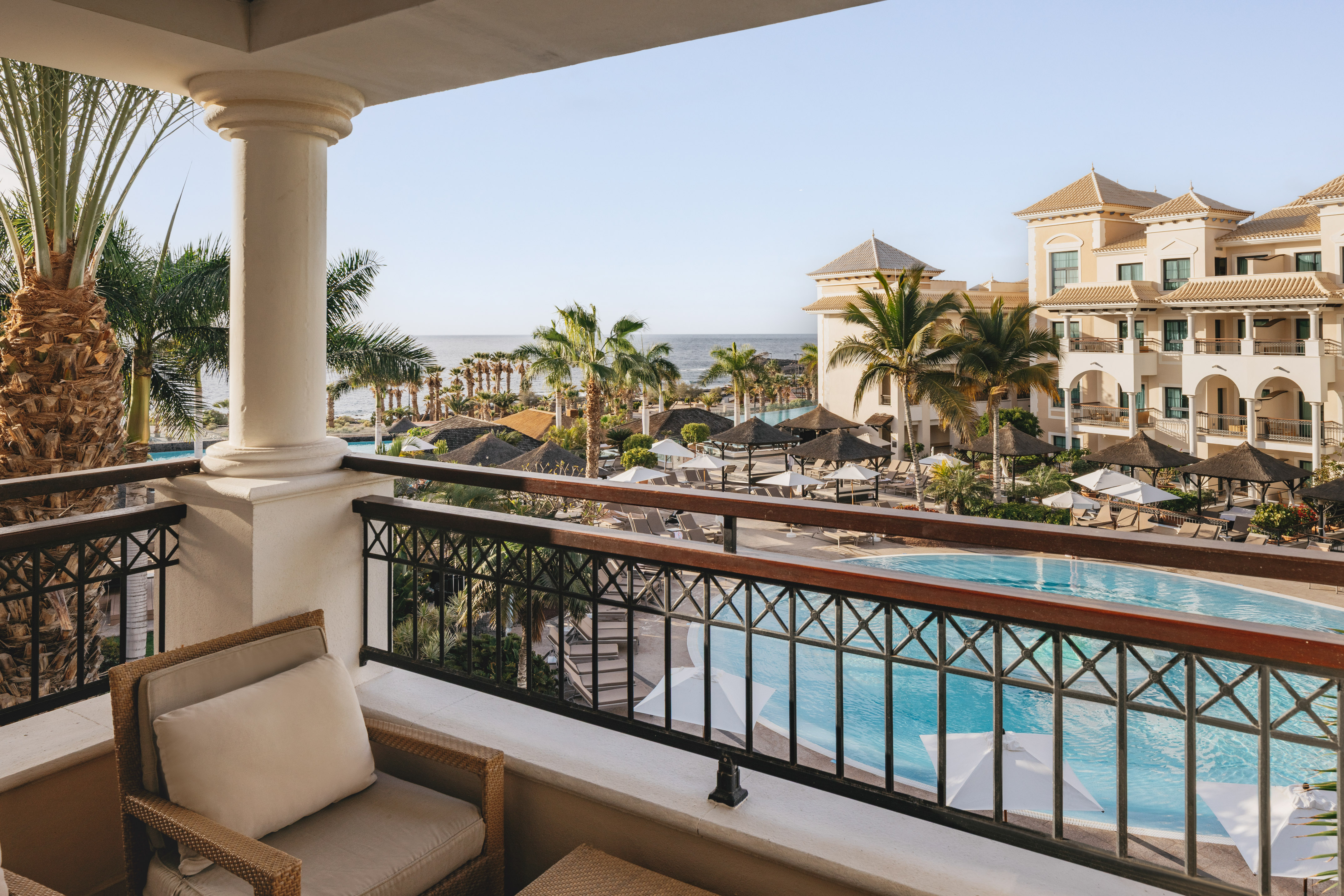 Luxury resort balcony with pool, palm trees, and ocean view.