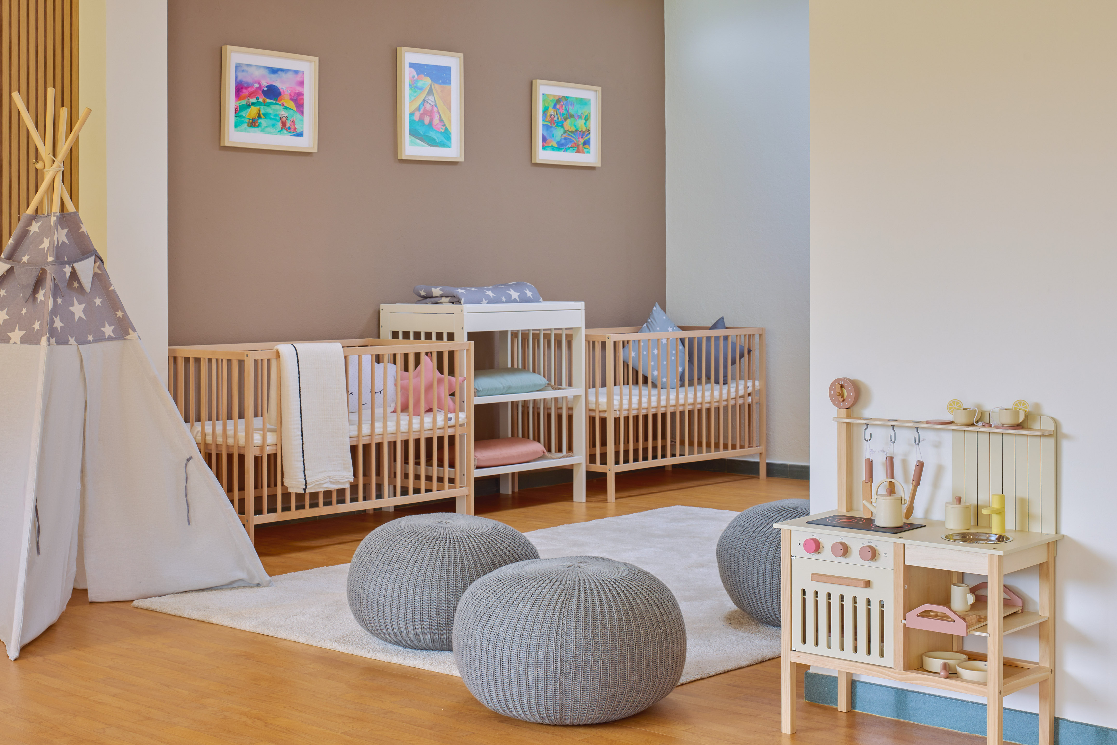 Modern baby nursery: multiple wooden cribs, star teepee, and play kitchen.