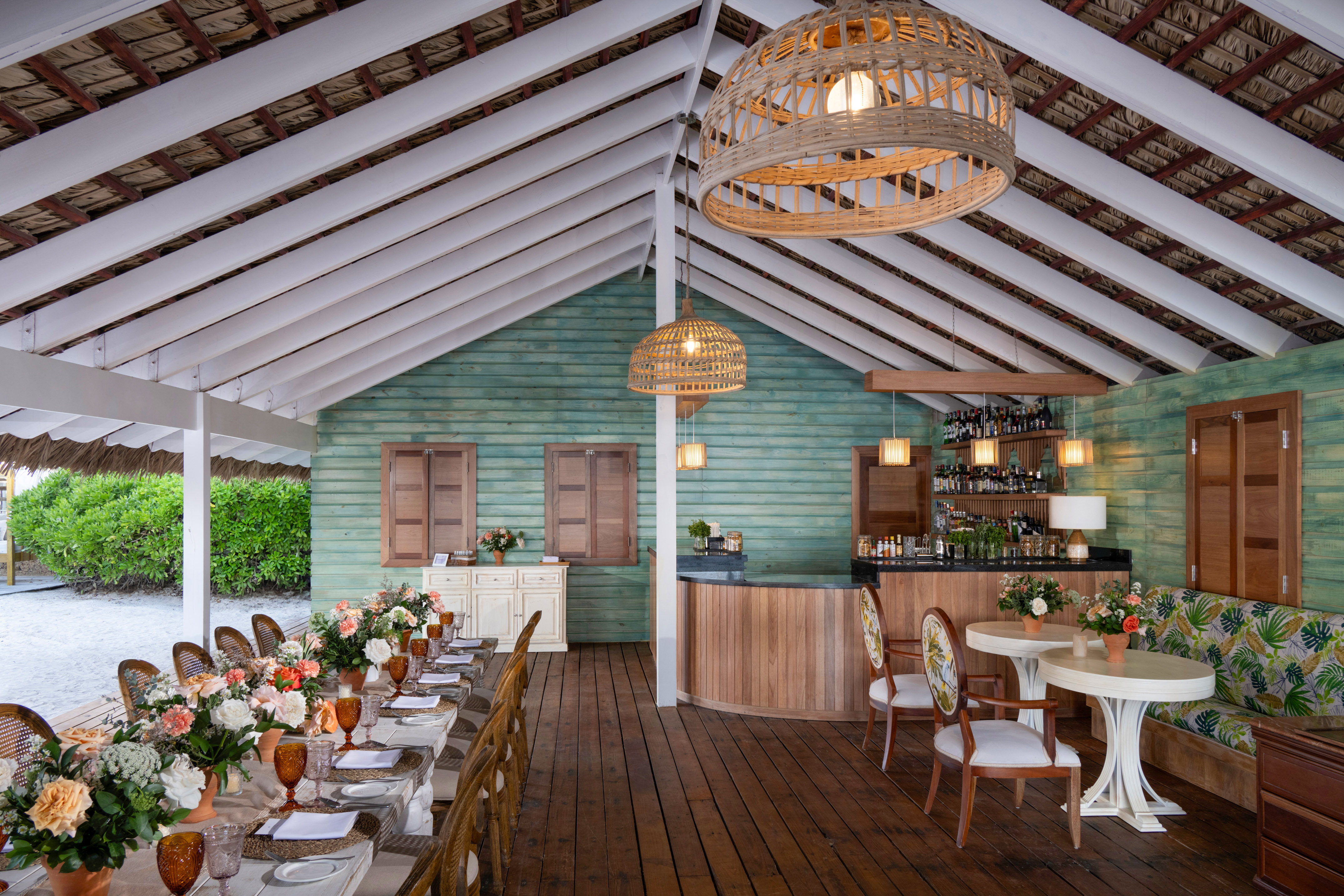 Beachfront restaurant with outdoor dining tables, bar, and rustic thatched roof.