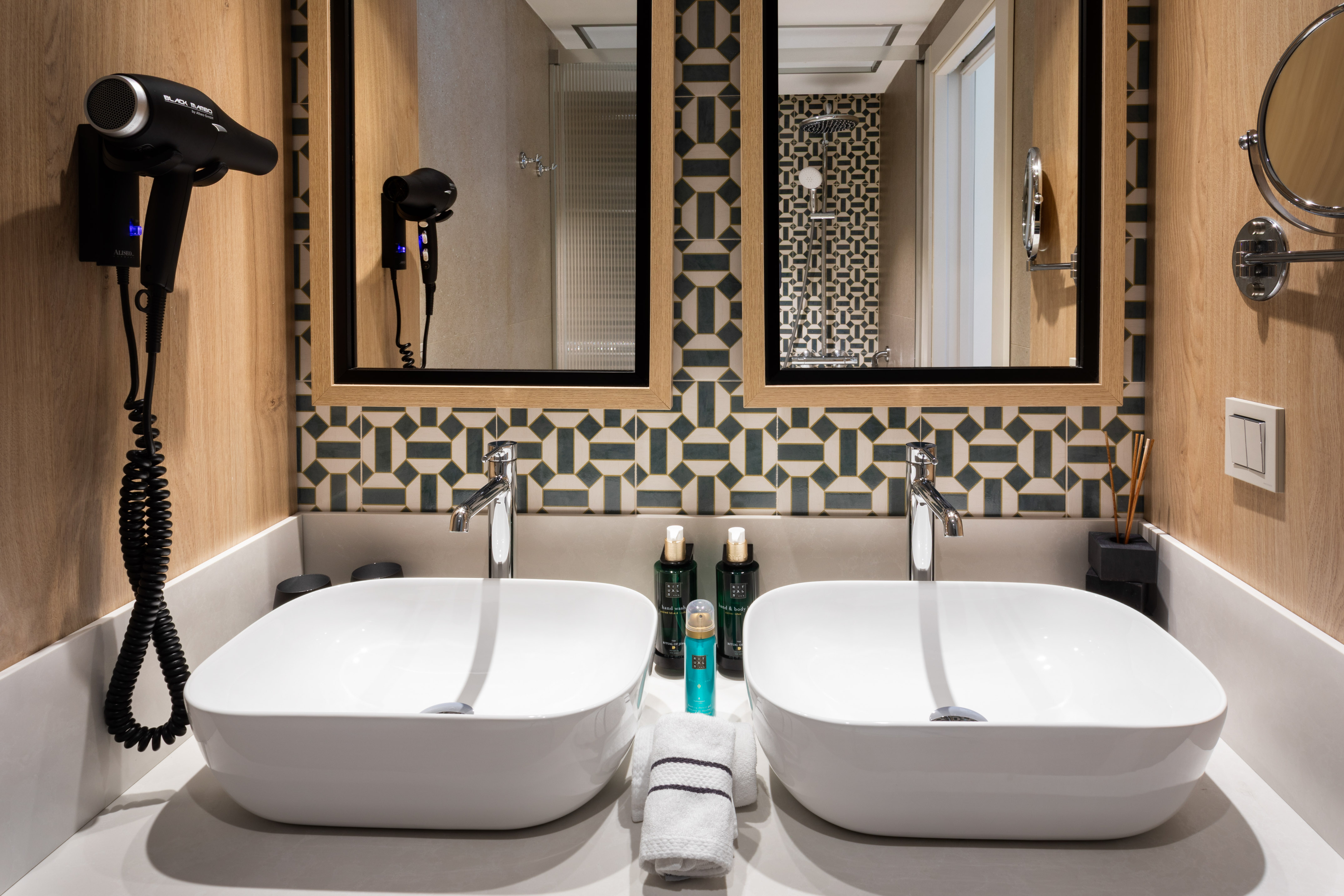 Modern hotel bathroom vanity with dual sinks, patterned backsplash, and hairdryer.