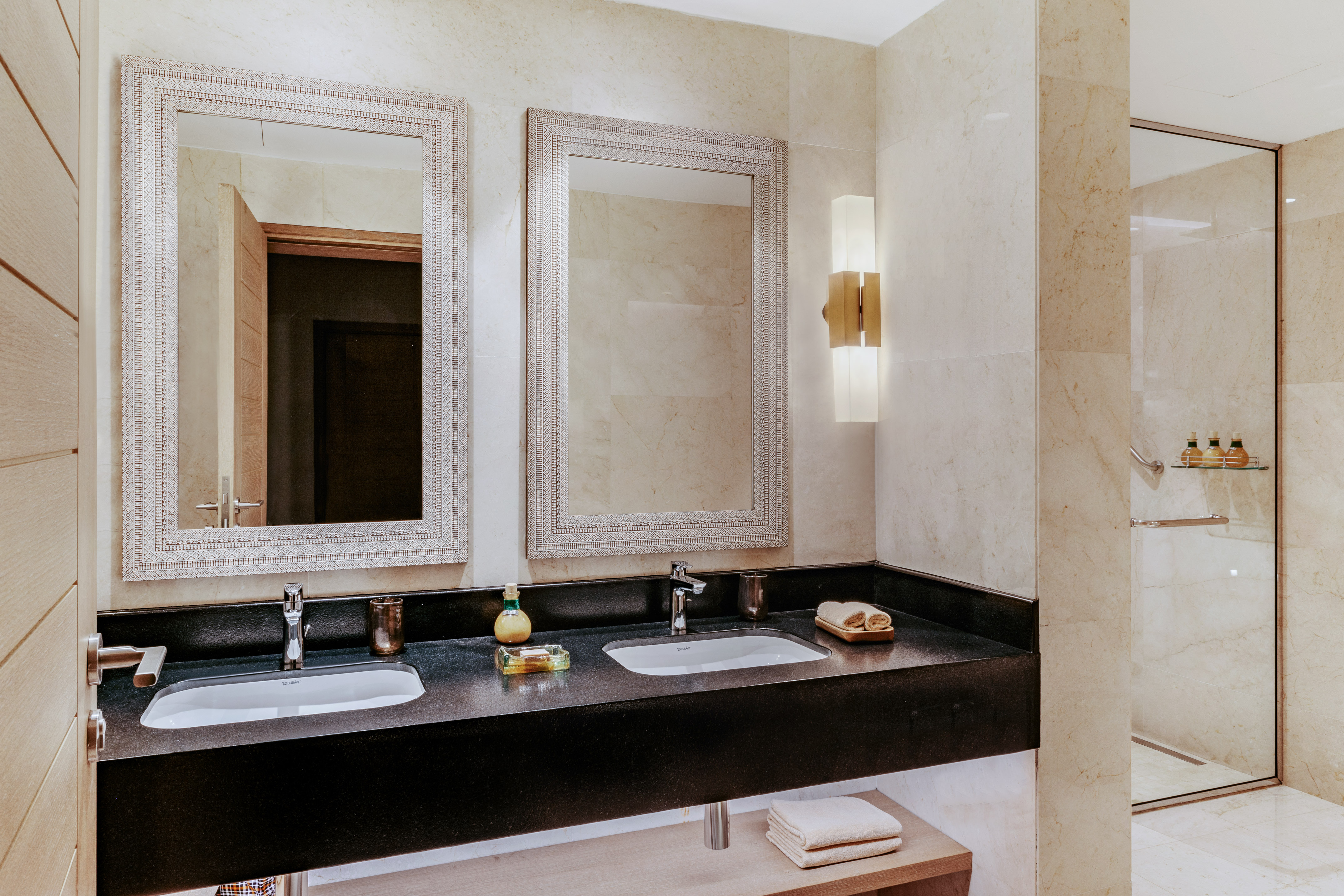 Luxury bathroom with double vanity, marble walls, and glass shower.