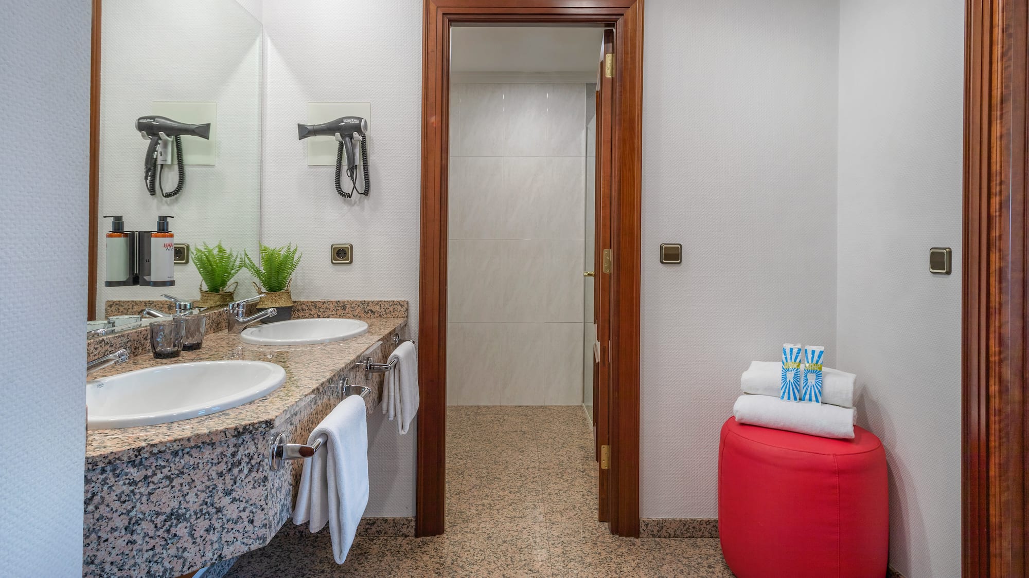 Hotel bathroom featuring double sinks, granite vanity, hairdryers, and clean towels.