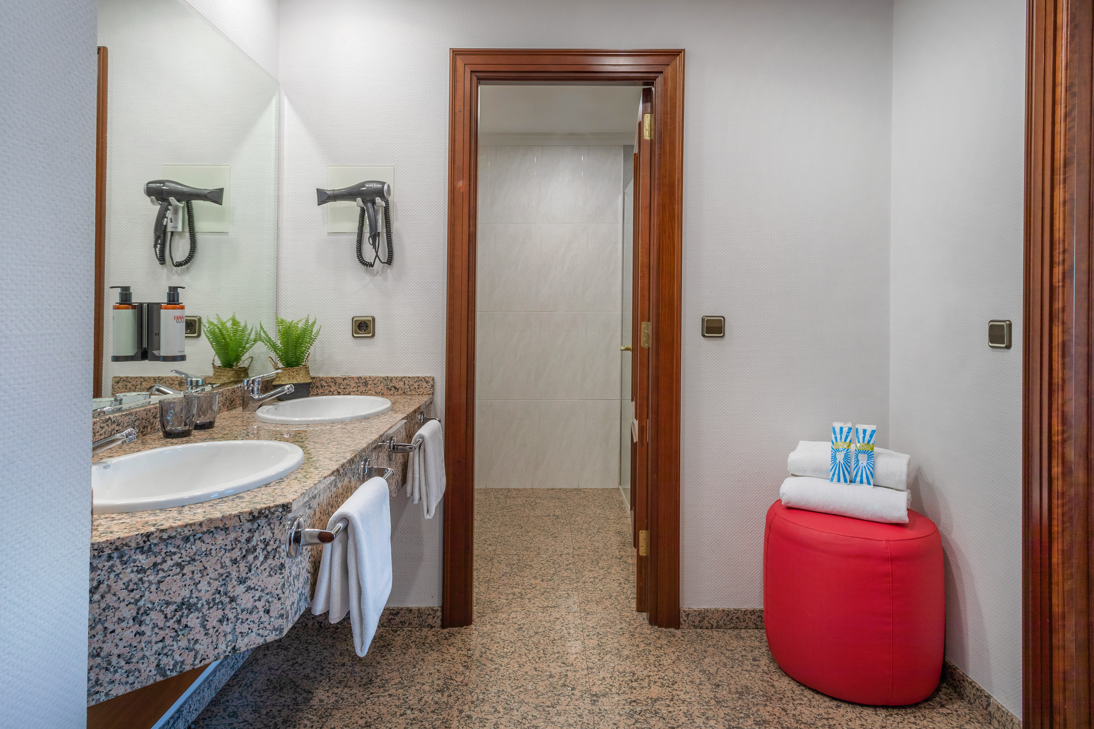 Hotel bathroom featuring double sinks, granite vanity, hairdryers, and clean towels.