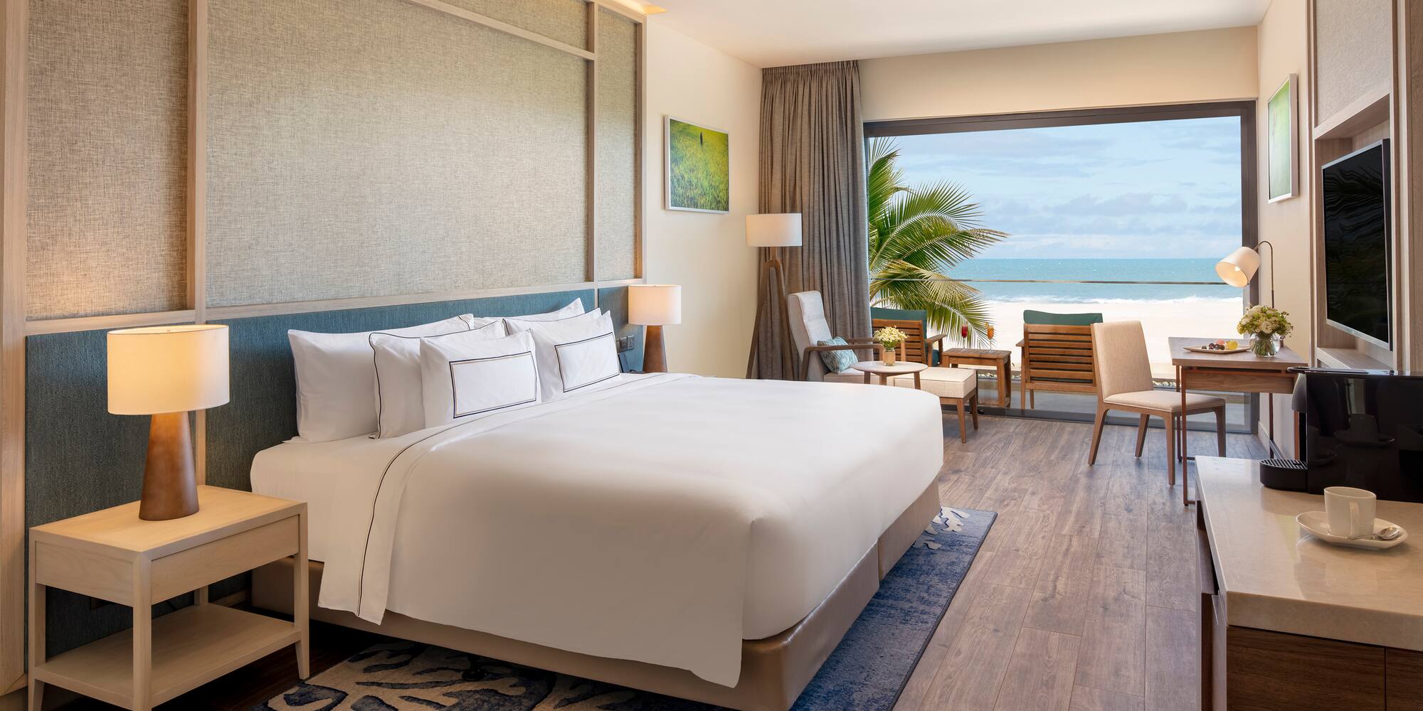Modern beachfront hotel room with ocean view, large bed, and balcony.