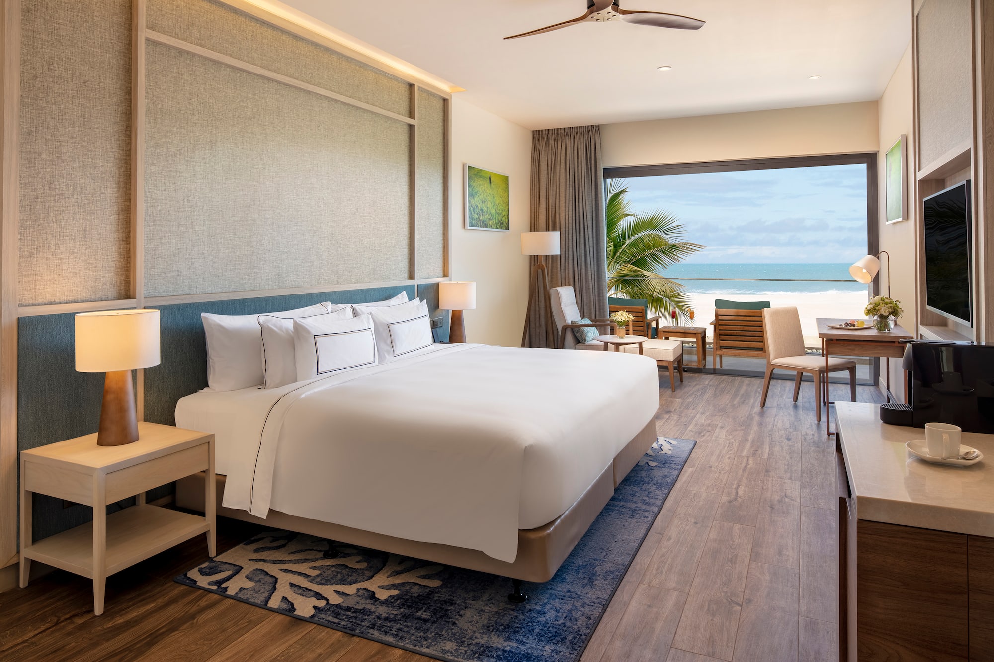 Modern beachfront hotel room with ocean view, large bed, and balcony.
