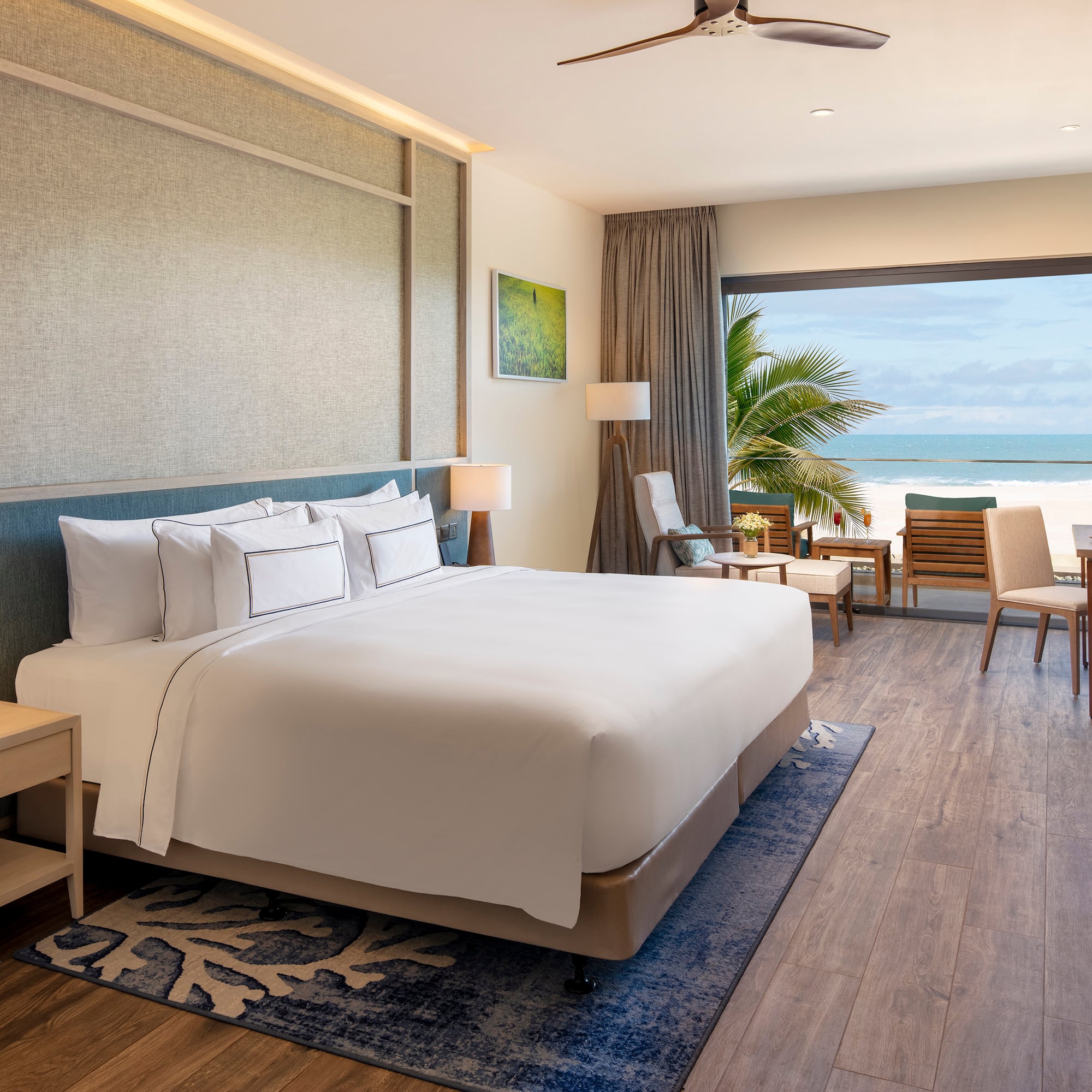 Modern beachfront hotel room with ocean view, large bed, and balcony.