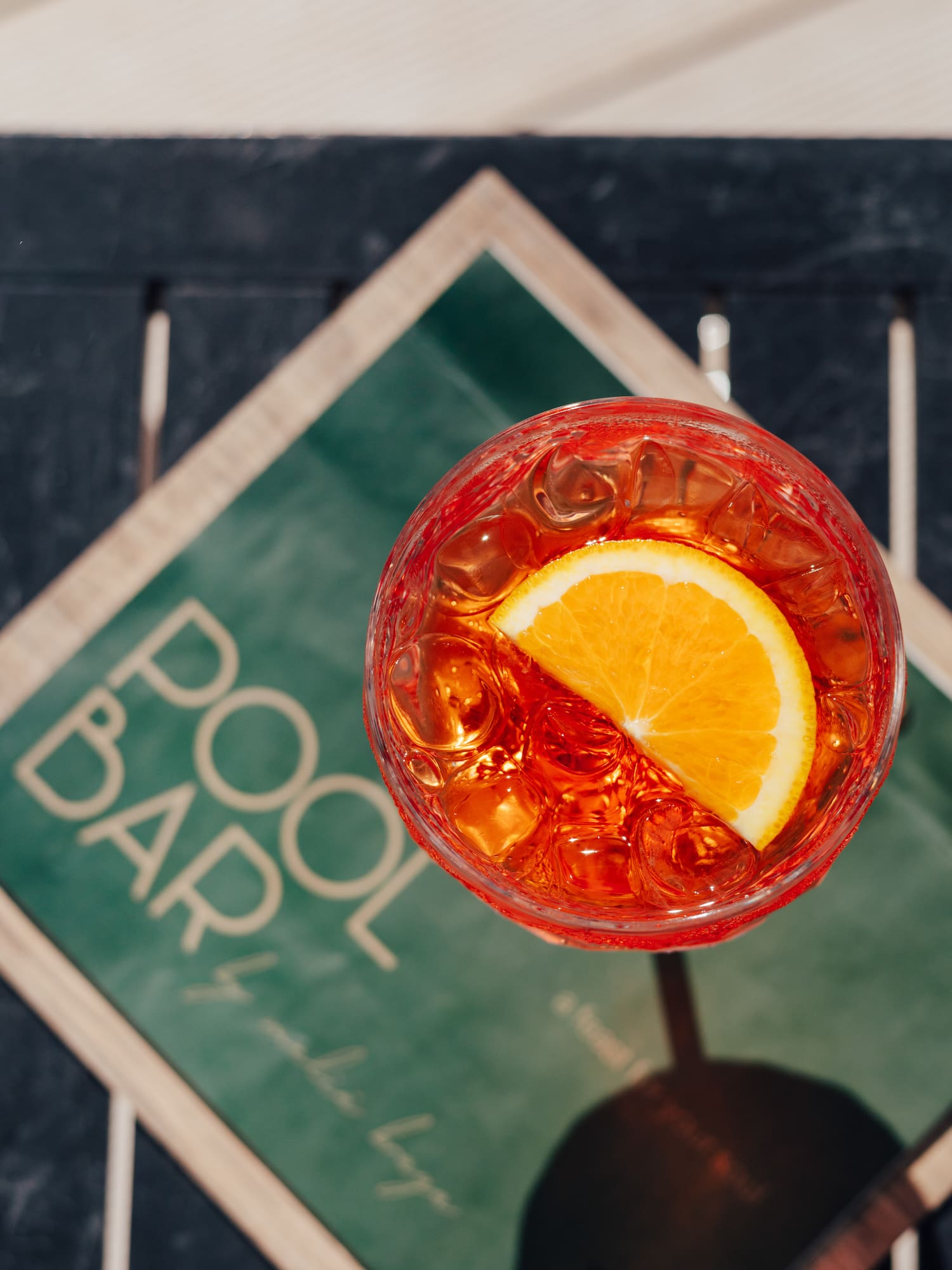 Aperol Spritz with orange slice and ice, on a table near a POOL BAR sign.