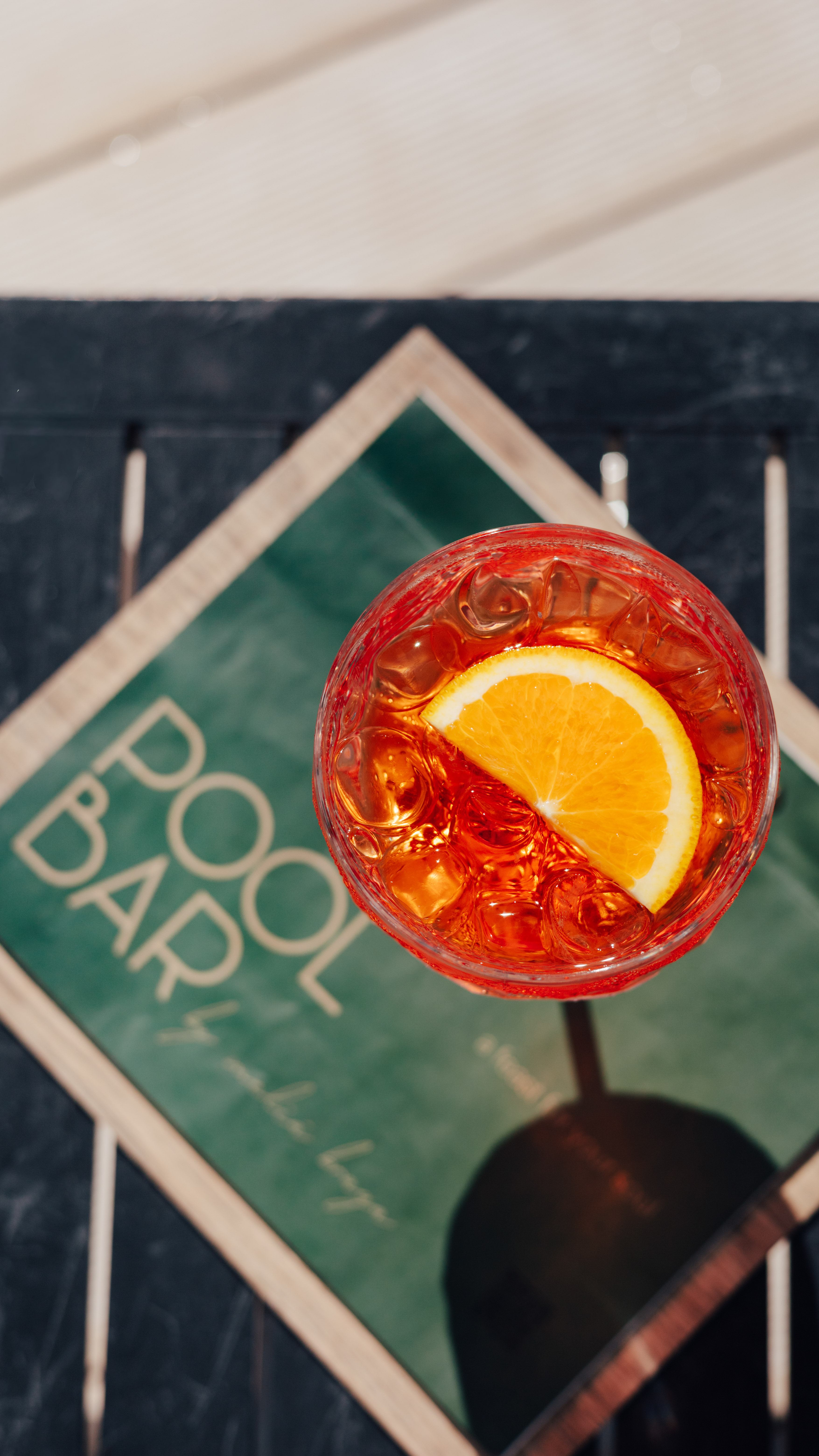 Aperol Spritz with orange slice and ice, on a table near a POOL BAR sign.