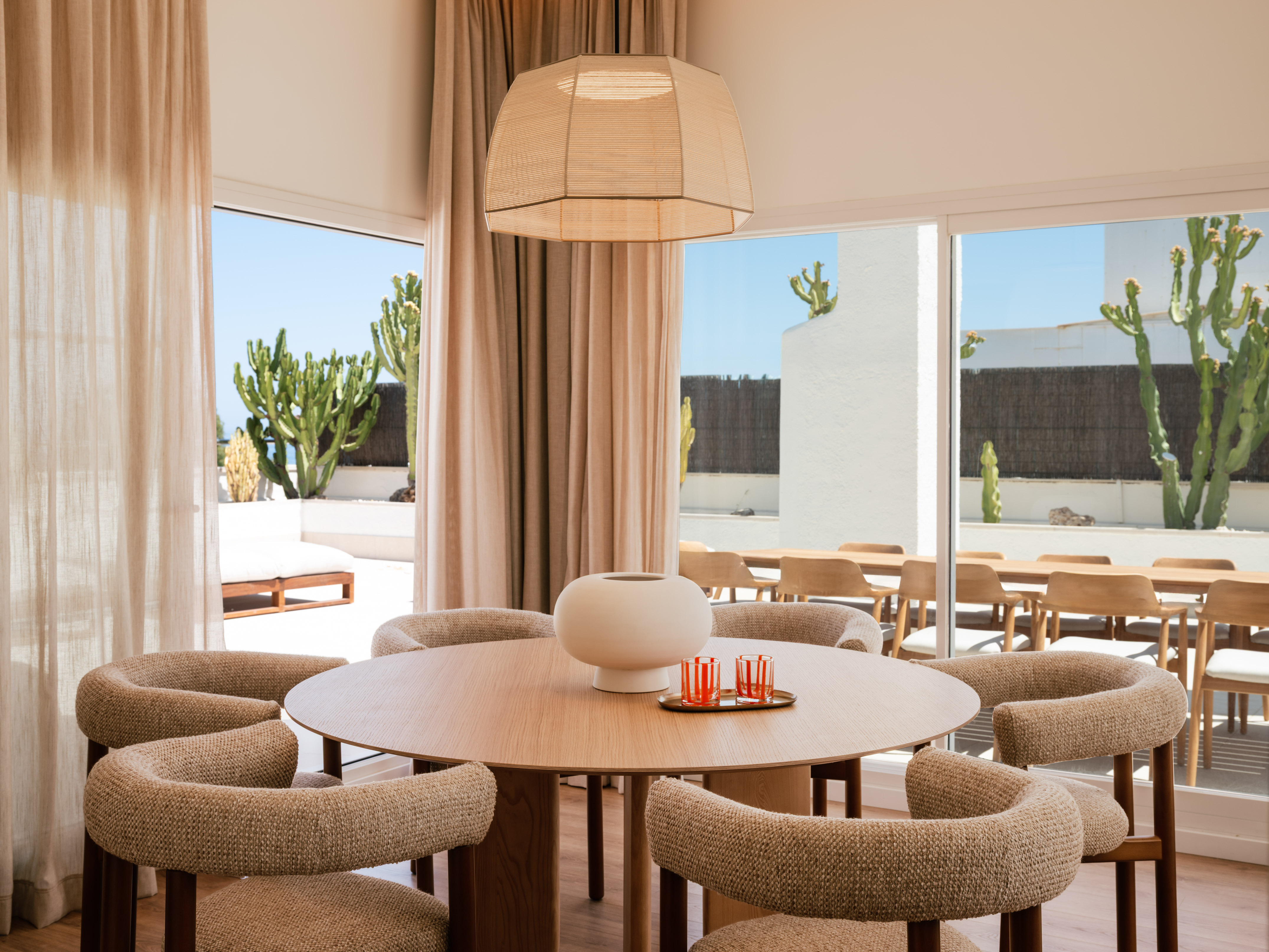 Bright dining room with round wood table, chairs, and outdoor cacti view.