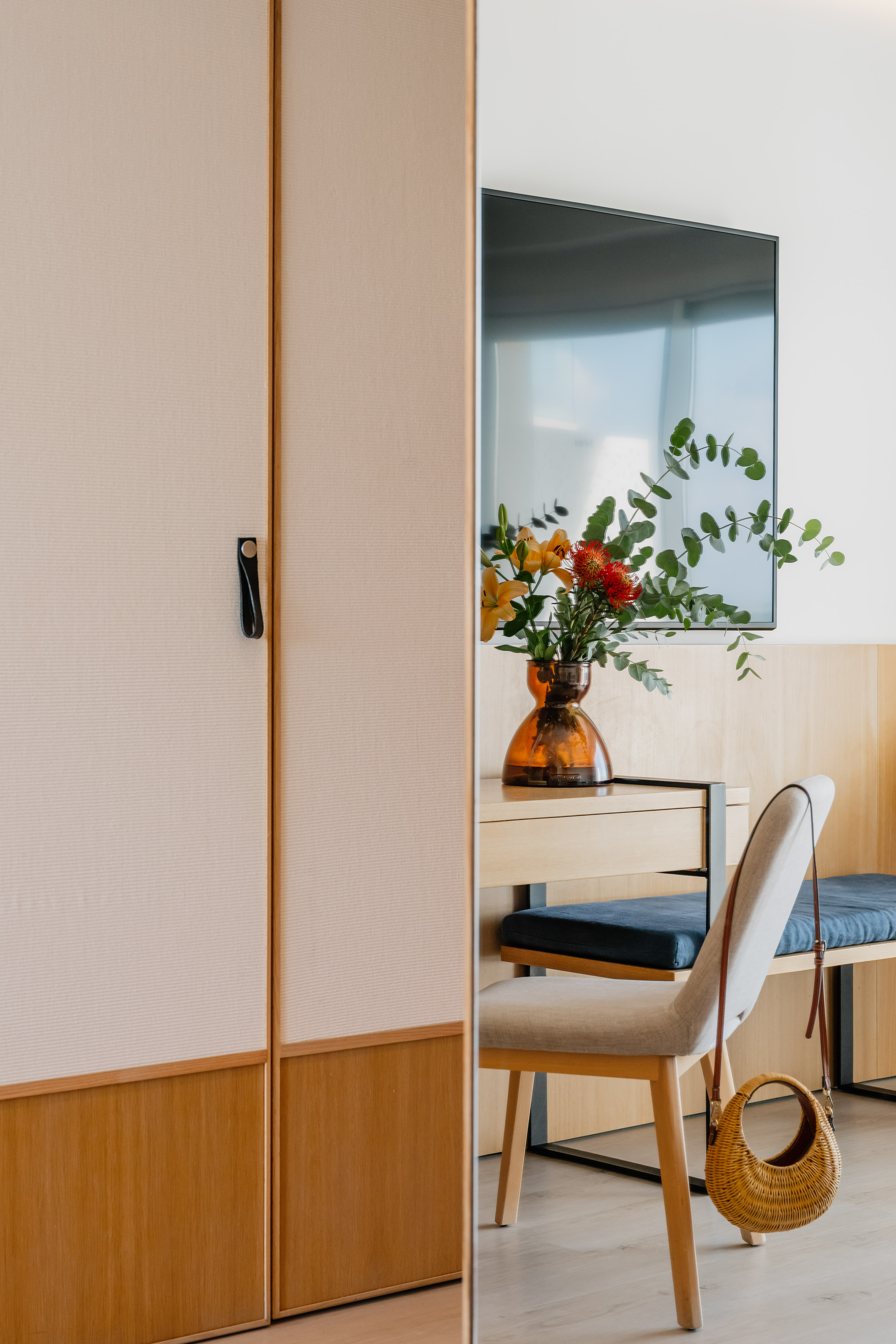 Elegant hotel room: beige wardrobe reflects modern desk, TV, colorful flowers.