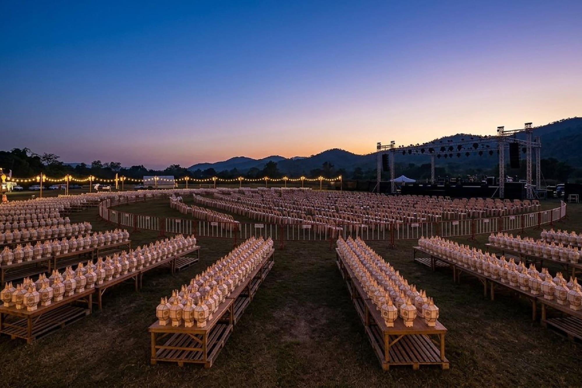 Outdoor lantern festival at twilight with white lanterns, stage, and mountains.