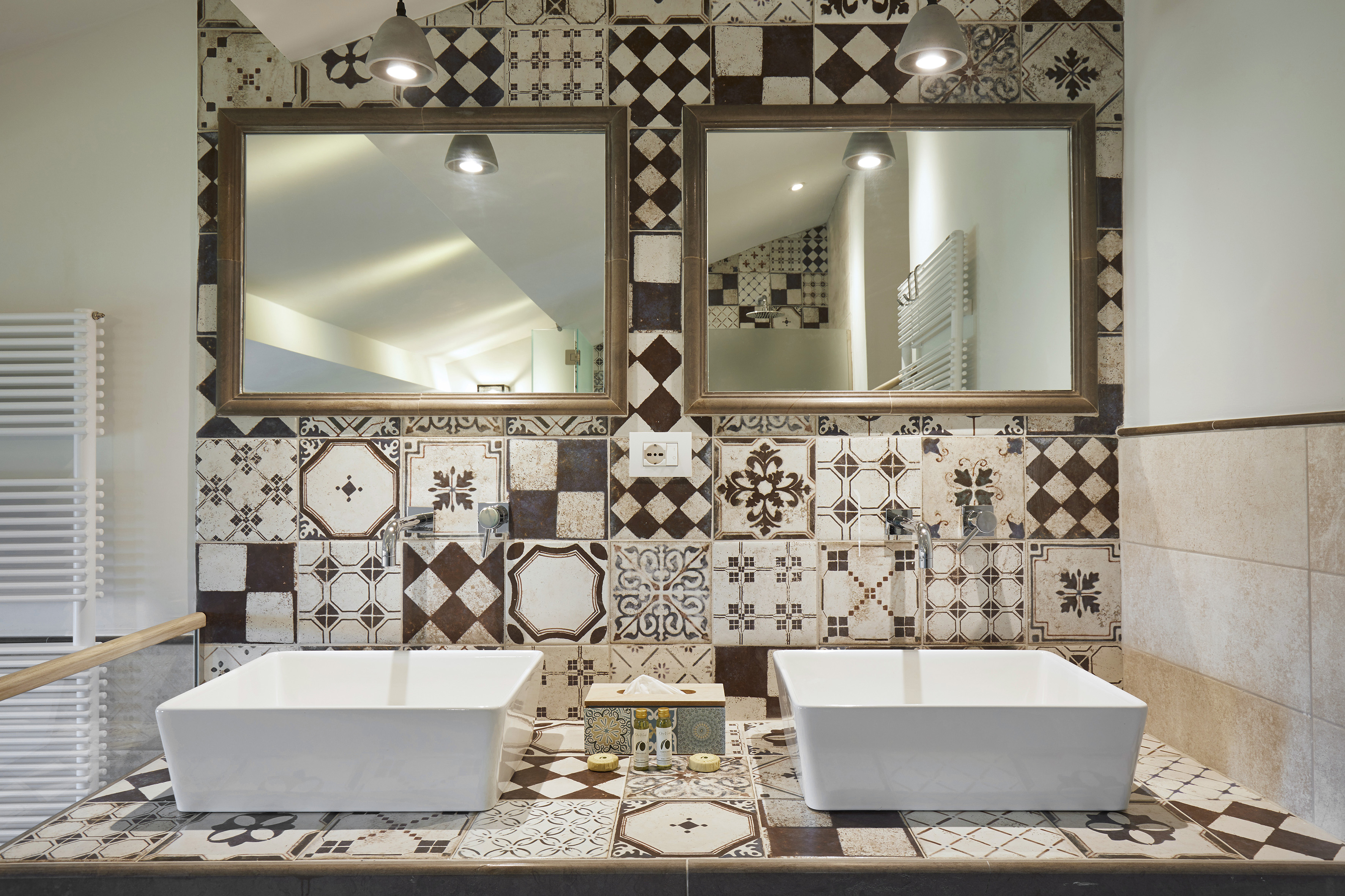 Double sink bathroom vanity with mirrors and ornate brown and white patterned tiles.