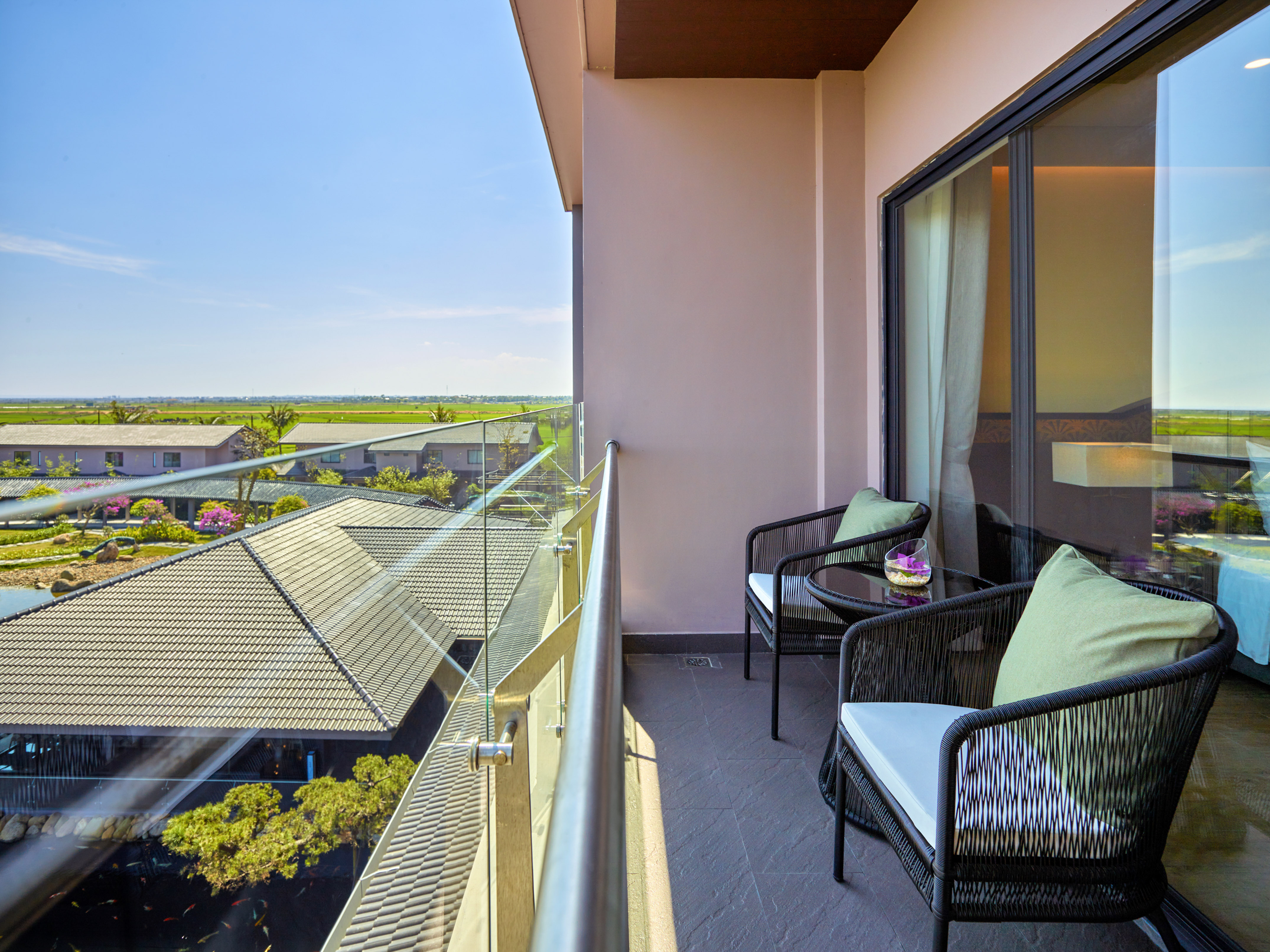 Resort balcony with chairs, glass railing, overlooking green rice fields and koi pond.