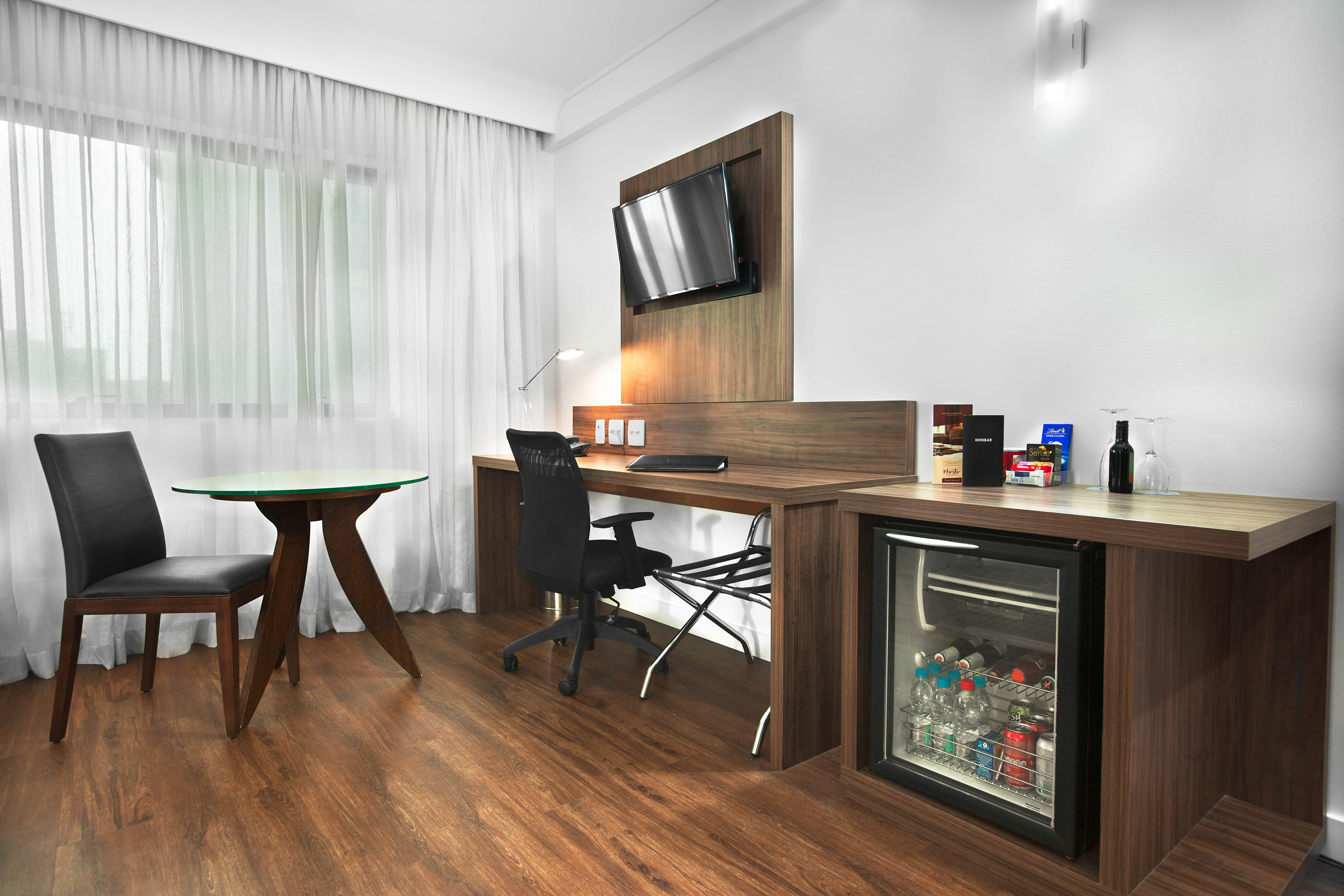 Modern hotel room workspace with desk, chair, TV, and minibar.