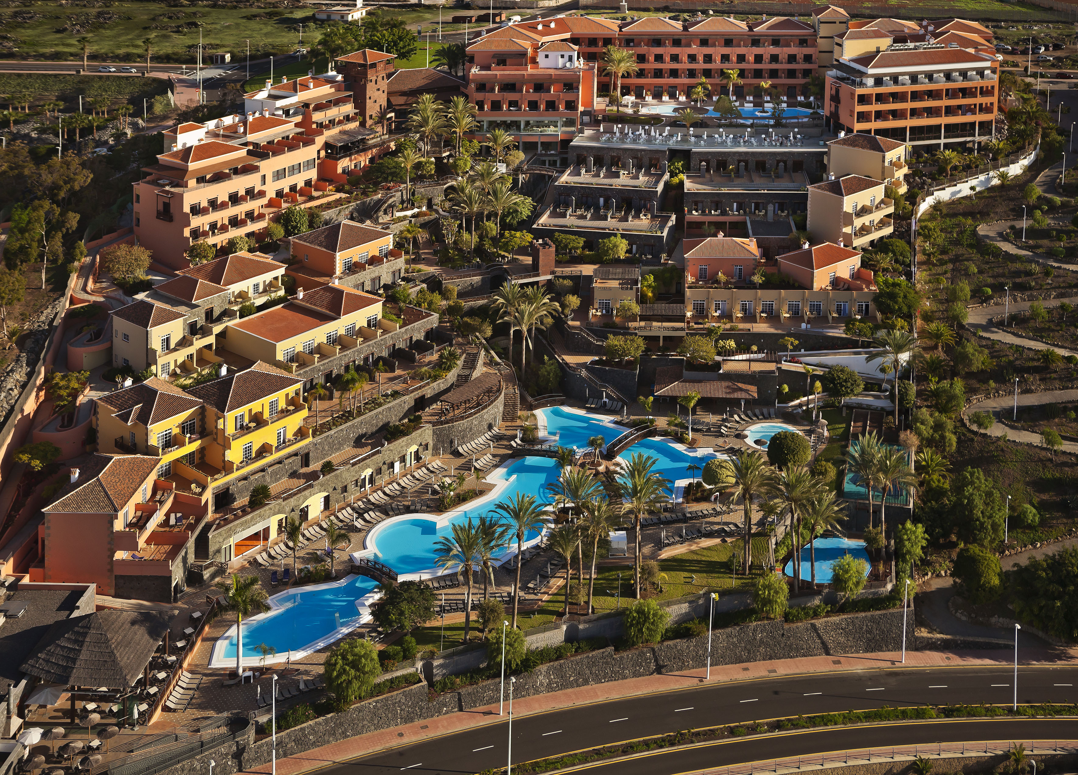 Aerial view: Resort hotel with multiple pools, palm trees, and terraced buildings.