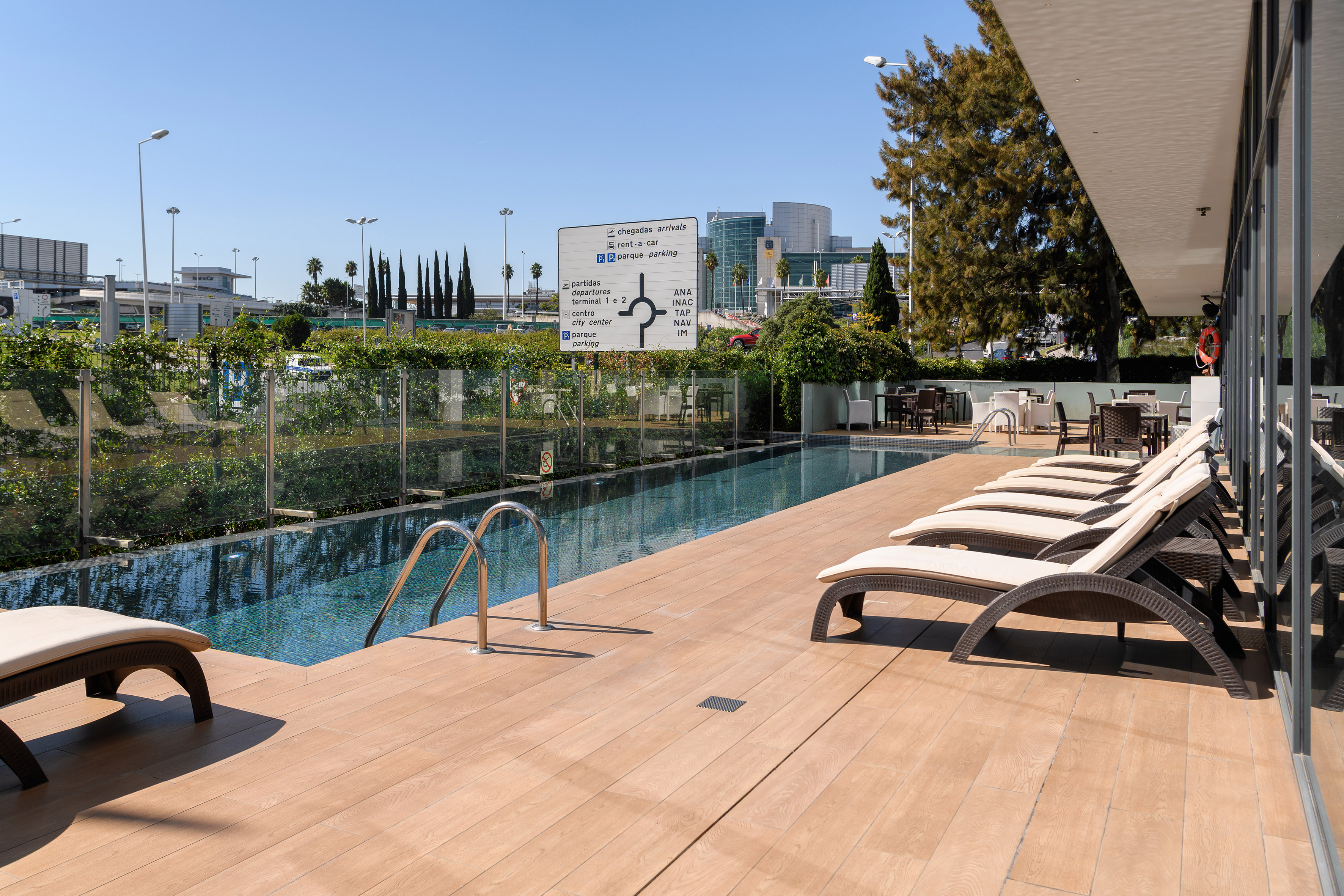 Airport hotel outdoor pool, sun loungers on wooden deck near terminal signs.