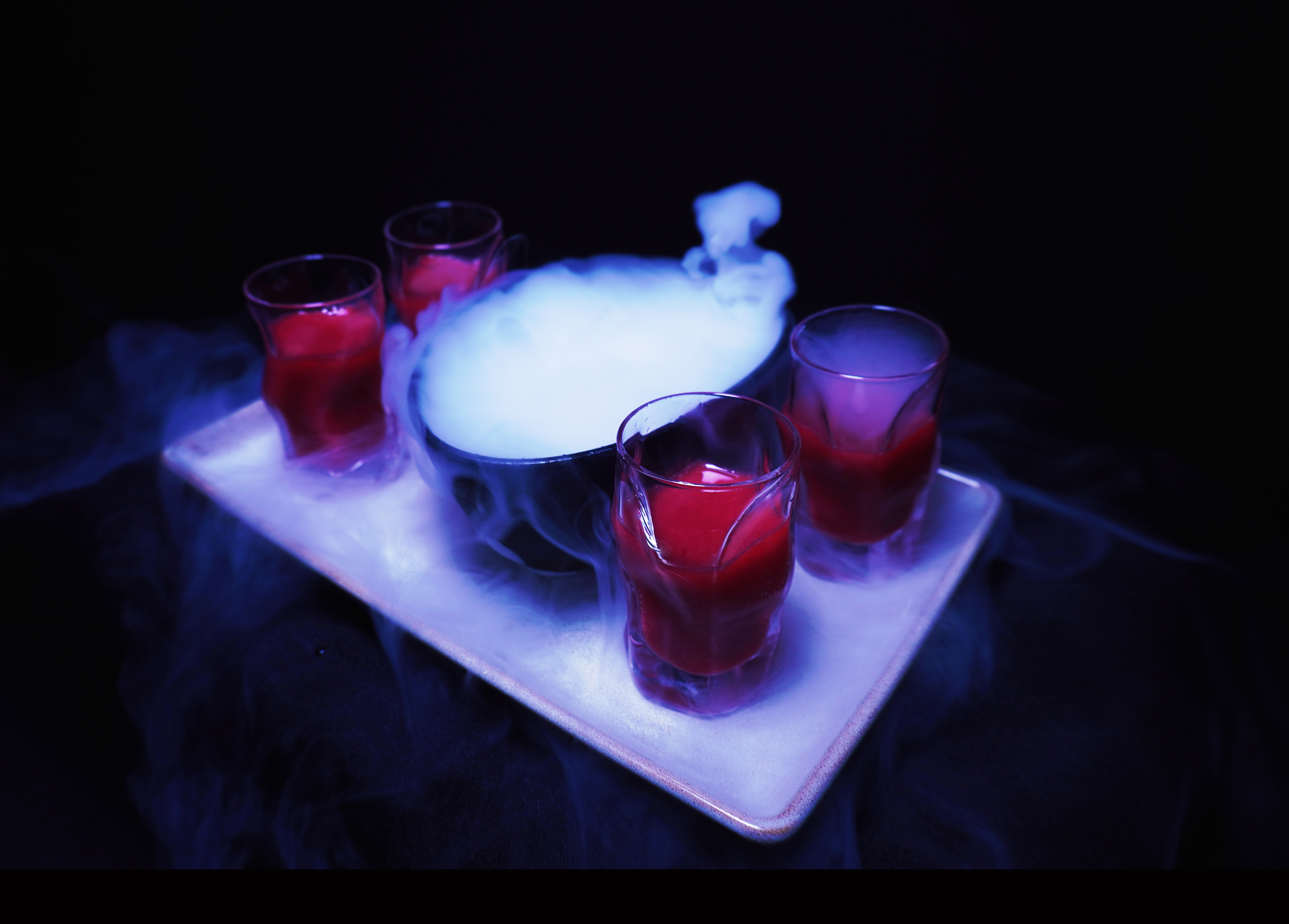 Red liquid shots with smoking dry ice on a tray, spooky Halloween drinks.